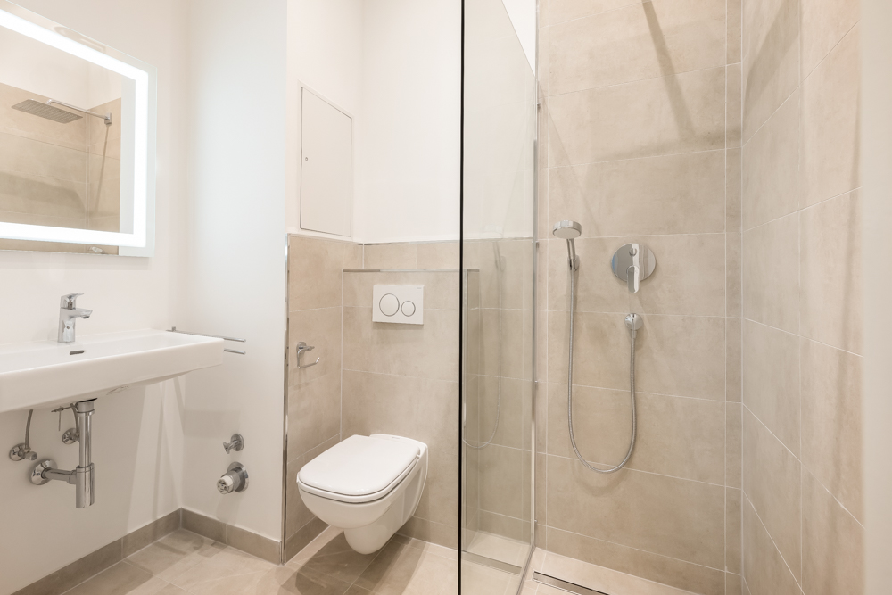 Modernes Bad mit begehbarer Dusche, Wandtoilette und breitem Waschbecken mit Spiegel.