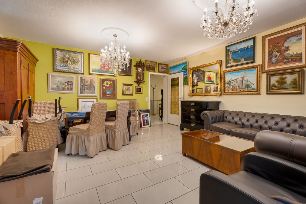 Wohnzimmer mit Ledersofa, Esstisch, Kronleuchtern und vielen Gemälden an den Wänden.