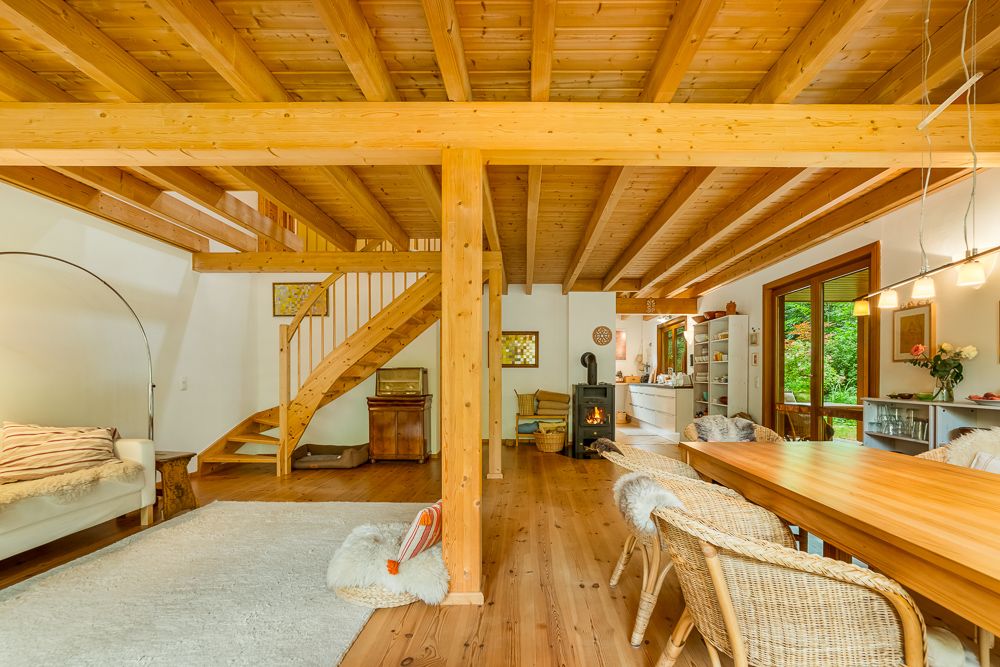 Helles Wohnzimmer mit Holzbalkendecke, Kamin, Esstisch und offener Treppe.