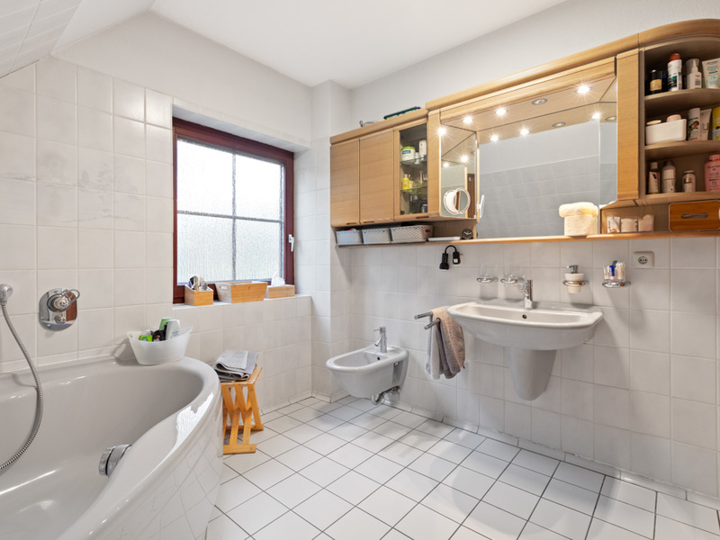 Helles Badezimmer mit Badewanne, Waschbecken, Bidet, Fenster und beleuchtetem Spiegelschrank.