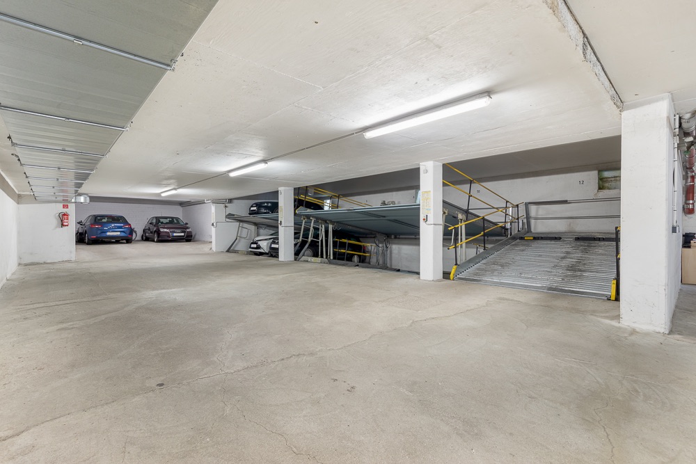 Helle Tiefgarage mit mehreren parkenden Autos und einem Doppelparksystem.