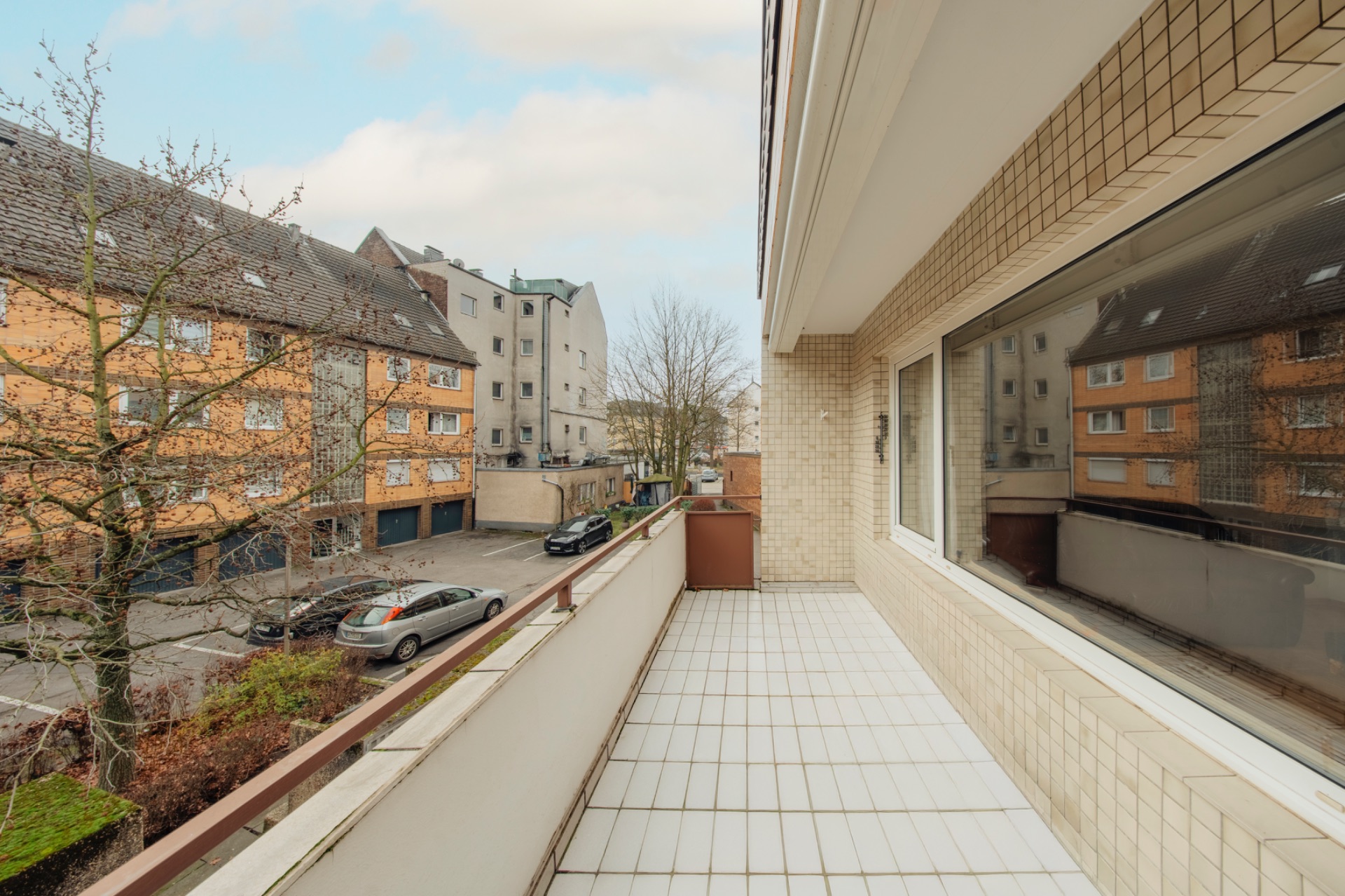 Balkon mit weißen Fliesen und Blick auf eine ruhige Wohnstraße mit geparkten Autos.
