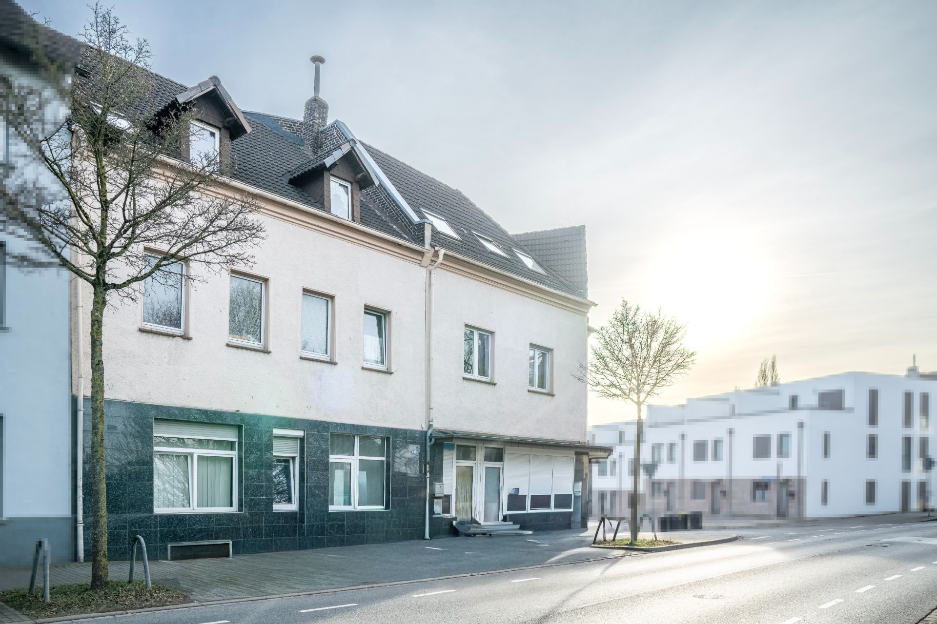 Wohnhaus mit mehreren Fenstern an einer ruhigen Straße bei Sonnenaufgang.