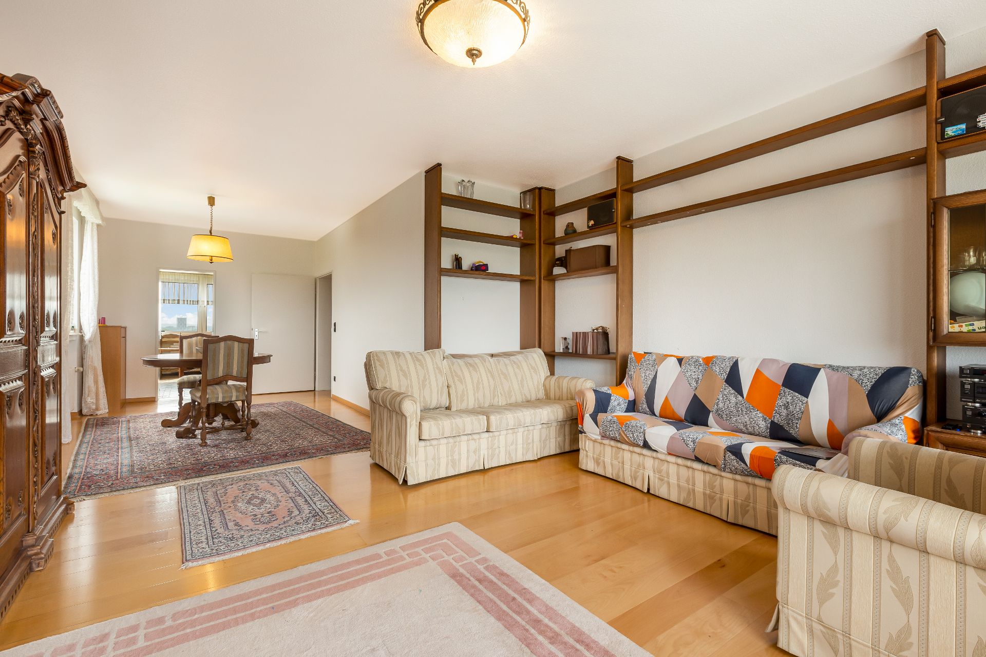 Wohnzimmer mit zwei Sofas, Holzregalen, Teppichen und Esstisch im Hintergrund.
