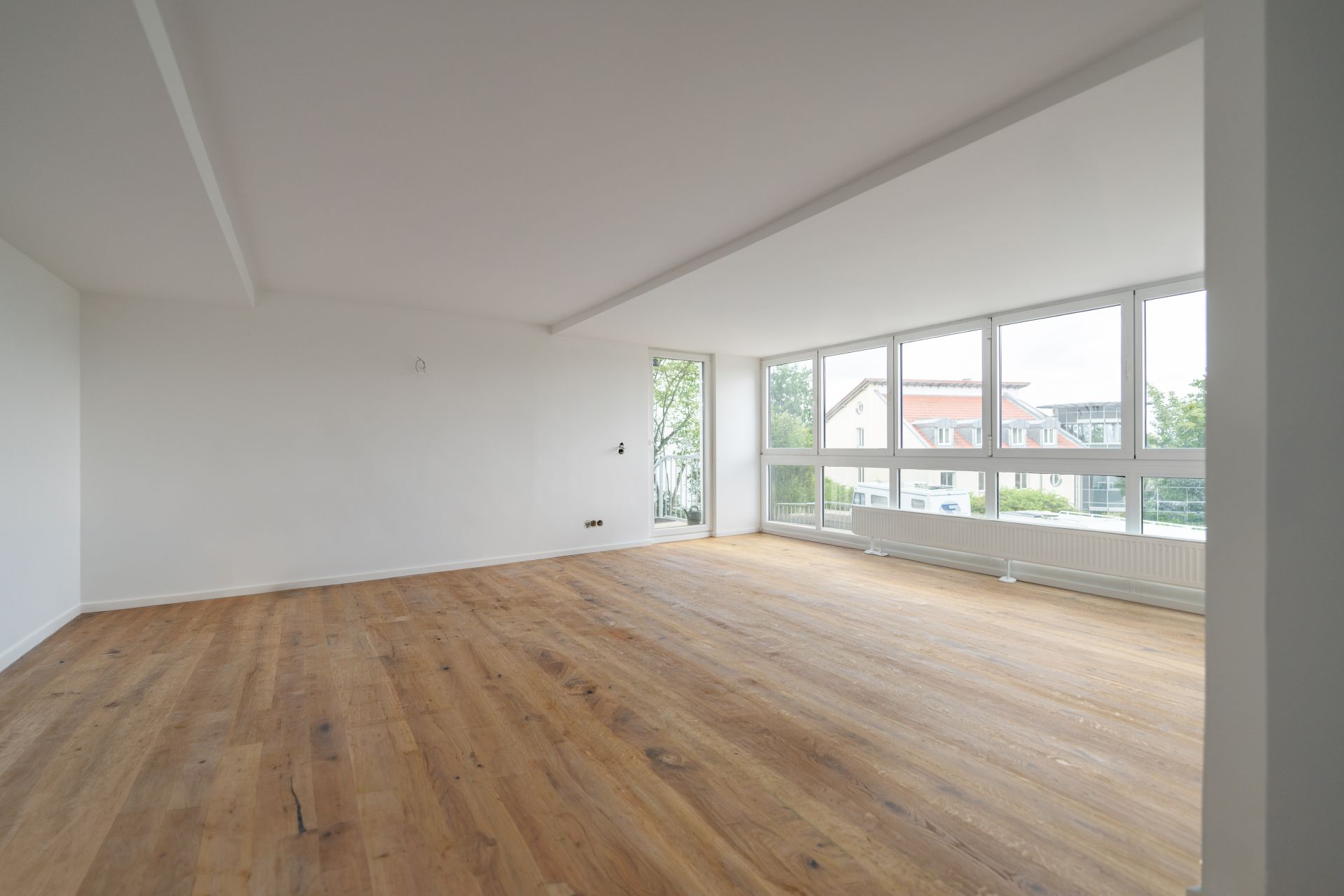 Helles, leeres Zimmer mit großen Fenstern und Holzboden.