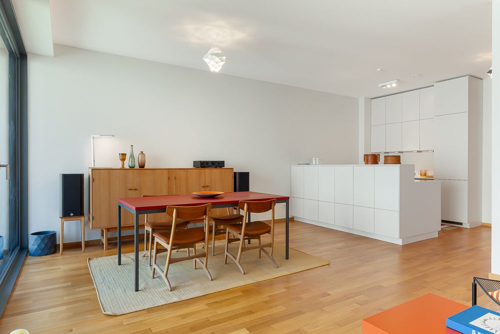 Offener Essbereich mit Holztisch, Stühlen und Sideboard, moderne weiße Küche im Hintergrund.