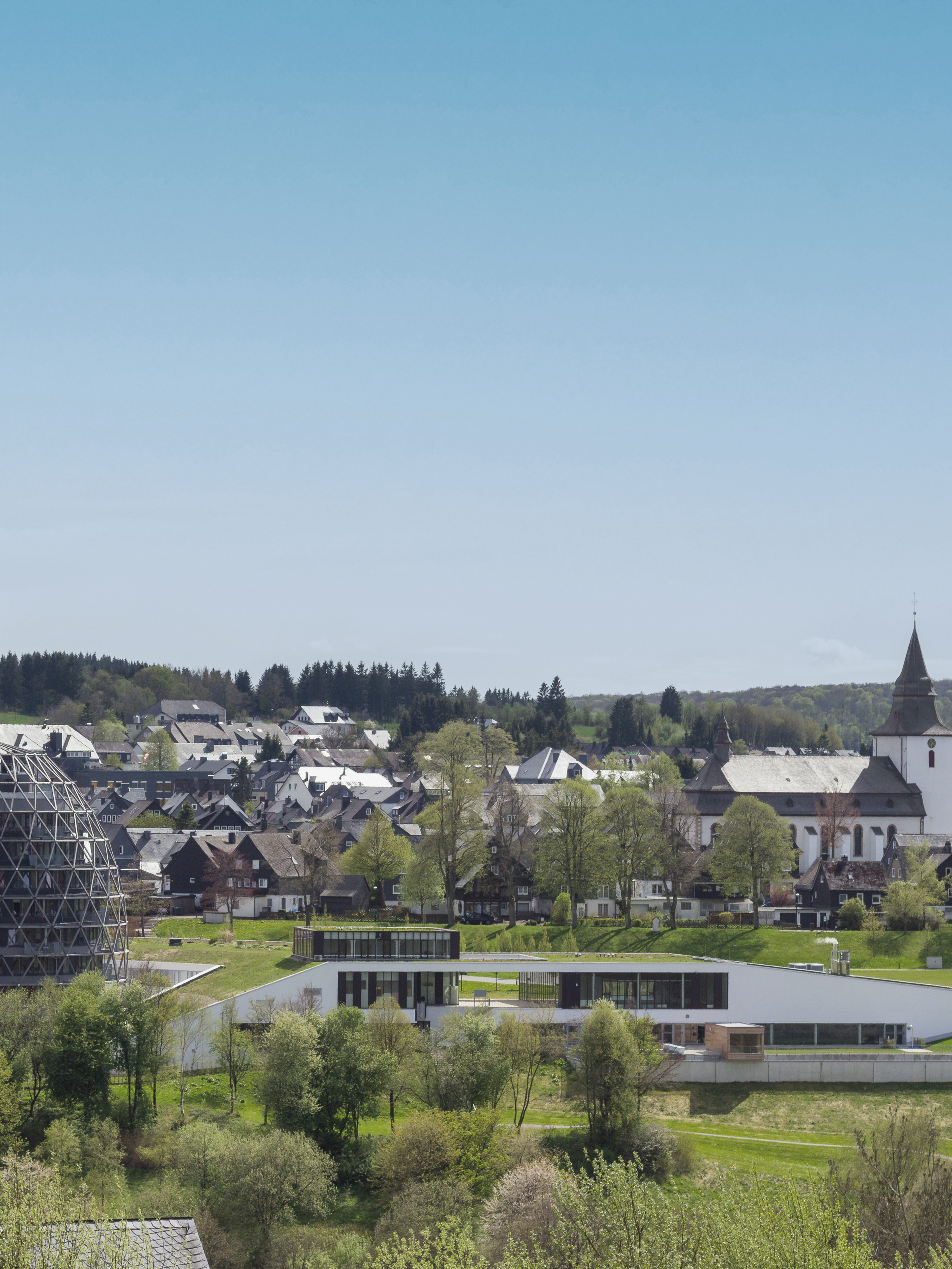 Blick auf ein Wohngebiet mit modernen und traditionellen Gebäuden, viel Grün und einer Kirche im Hintergrund.