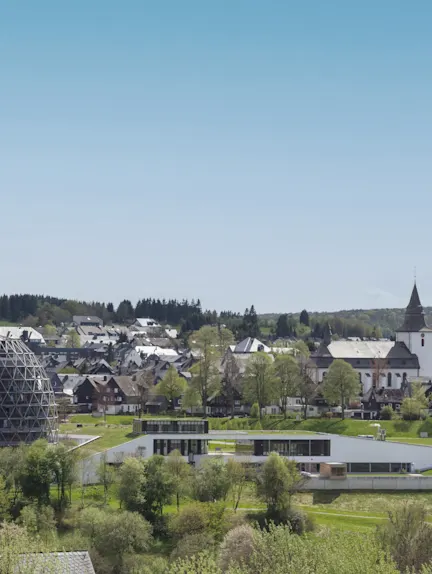 Blick auf ein Wohngebiet mit modernen und traditionellen Gebäuden, viel Grün und einer Kirche im Hintergrund.