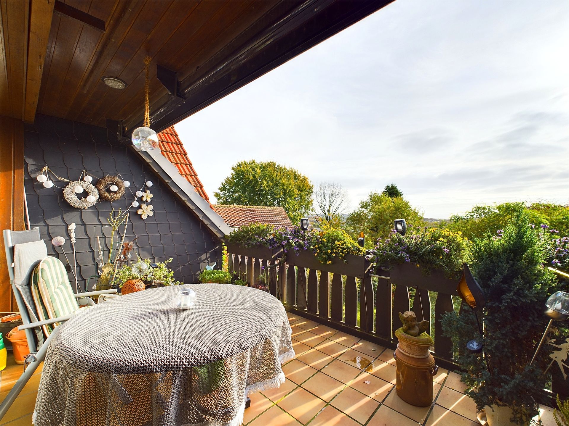 Balkon mit rundem Tisch, Stuhl, Pflanzen und Blumenkästen, Blick ins Grüne.
