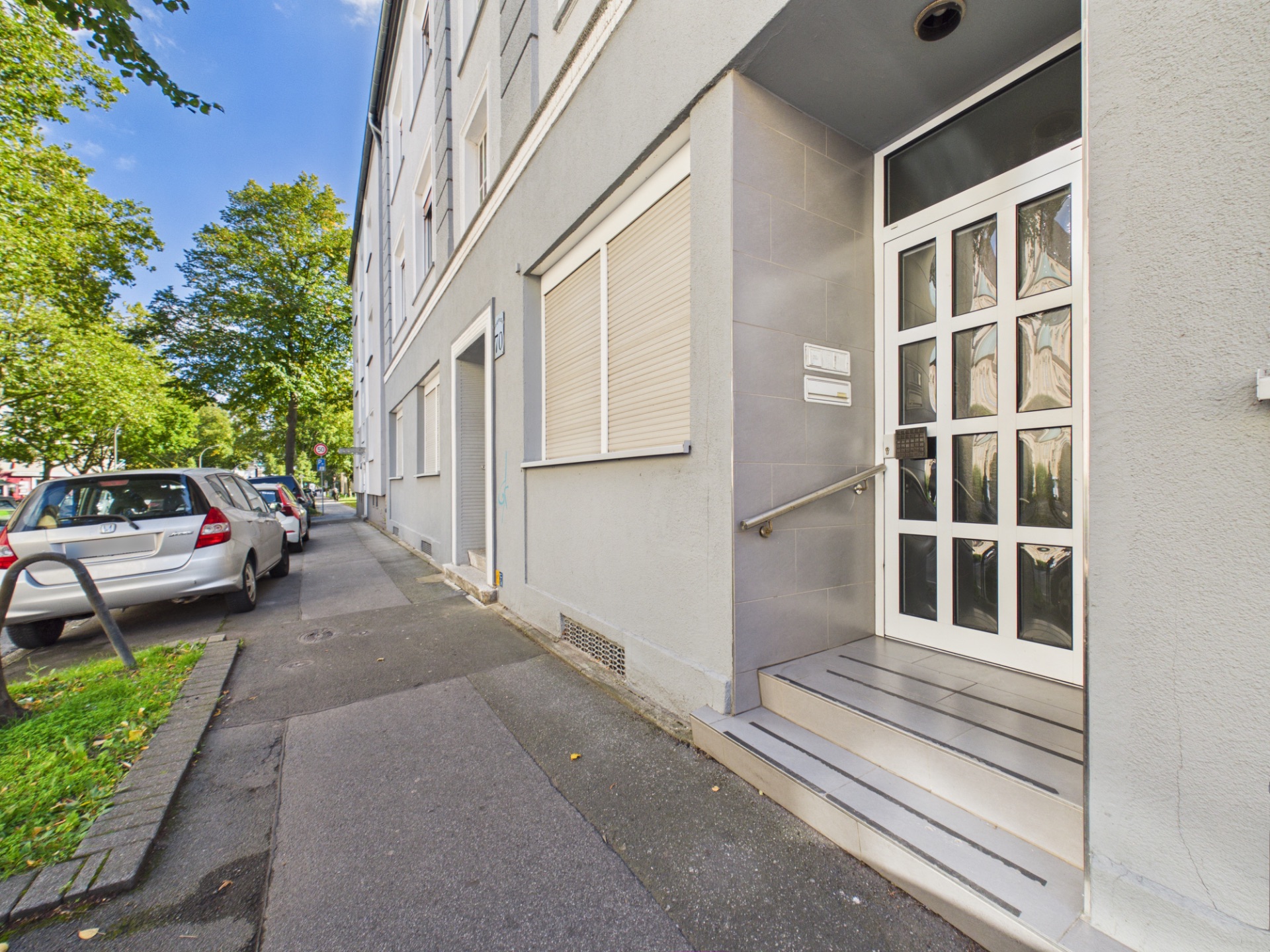 Eingangstür eines Wohnhauses mit Treppe und Handlauf an einer ruhigen Straße.