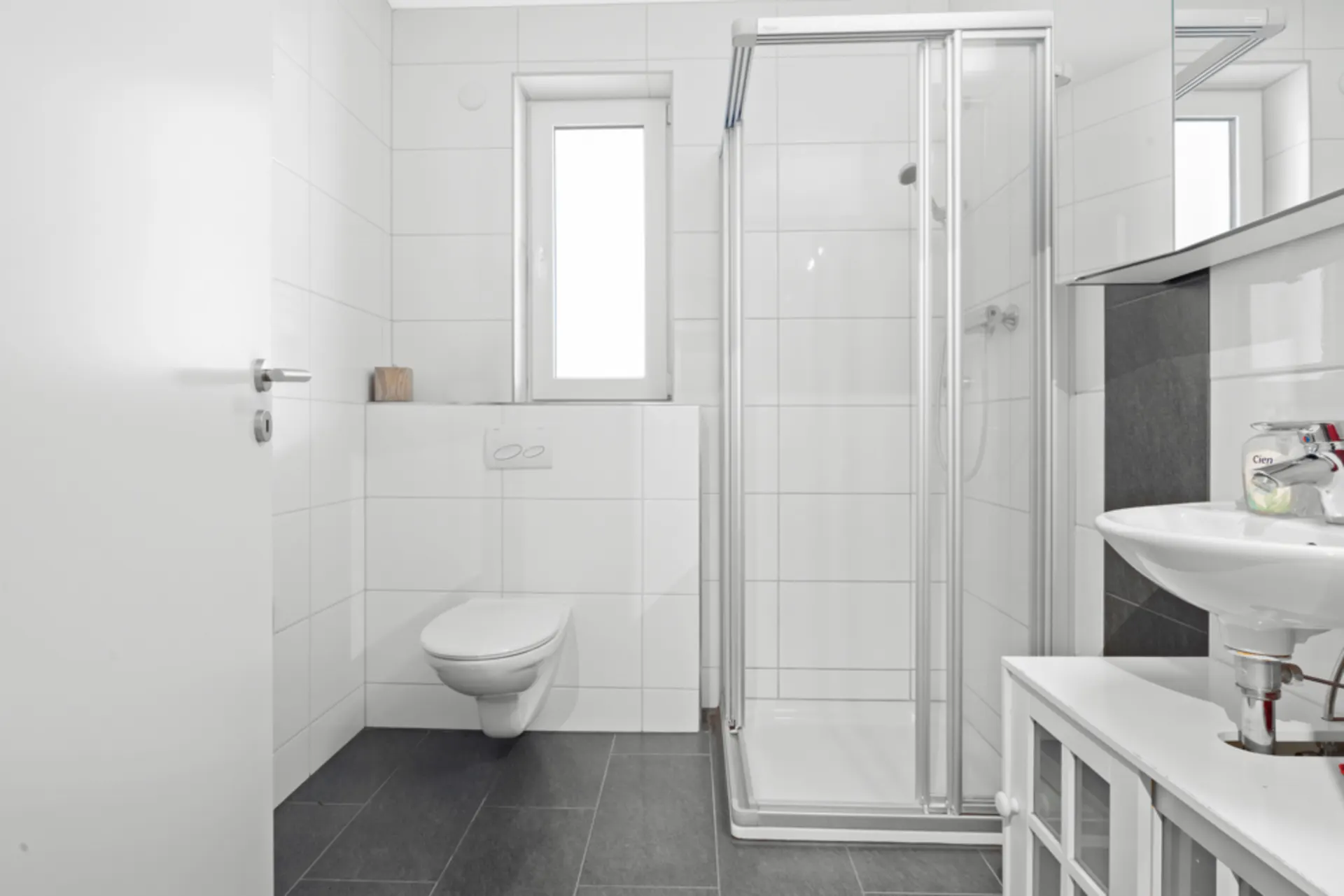 Modernes Badezimmer mit Dusche, WC, Fenster und Waschbecken mit Spiegel.