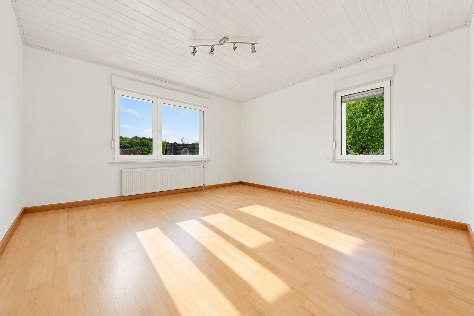 Heller leerer Raum mit zwei Fenstern, Holzfußboden und weißer Decke.