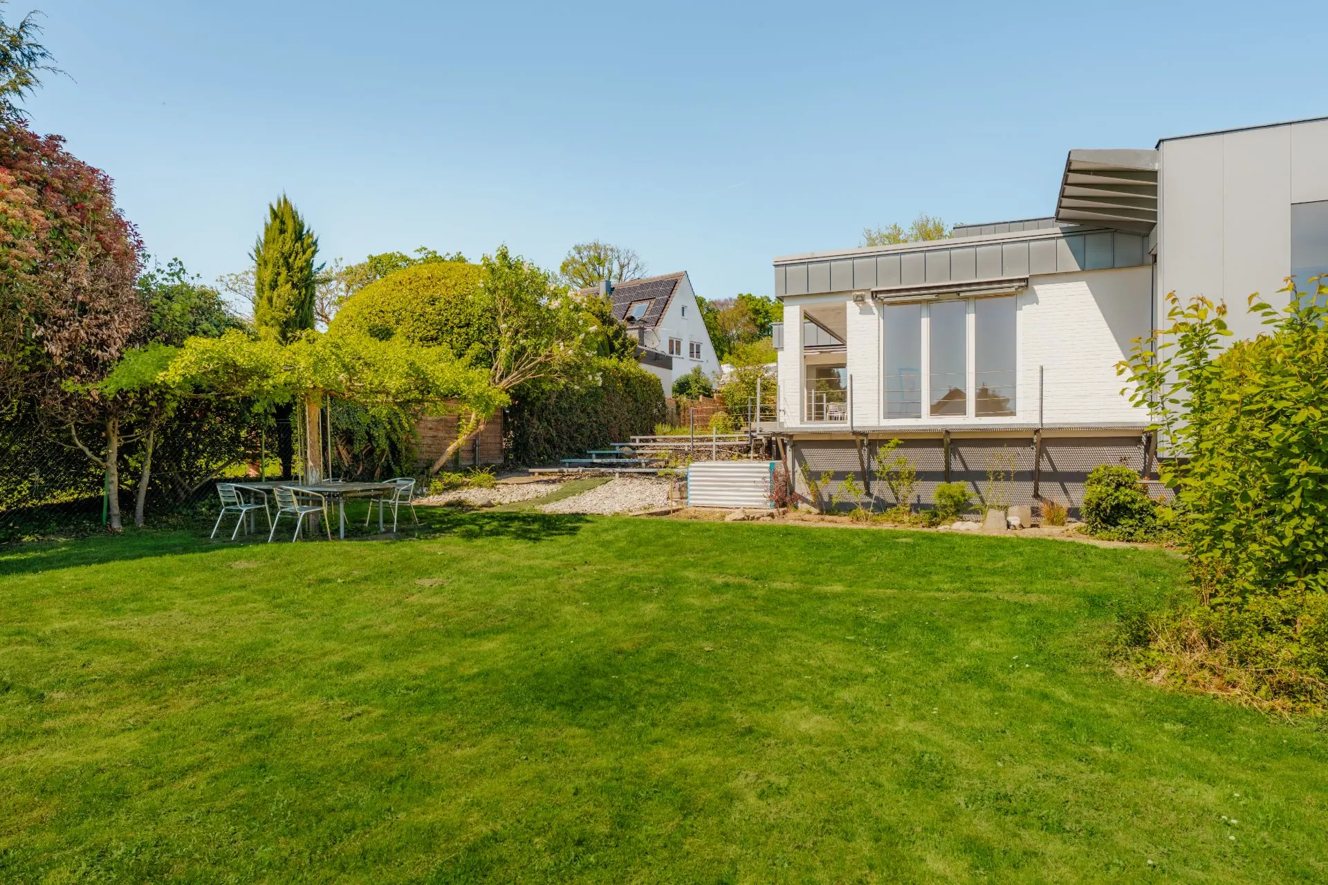 Großer Garten mit Rasen, Terrasse, Gartenmöbeln und modernem Haus im Hintergrund.