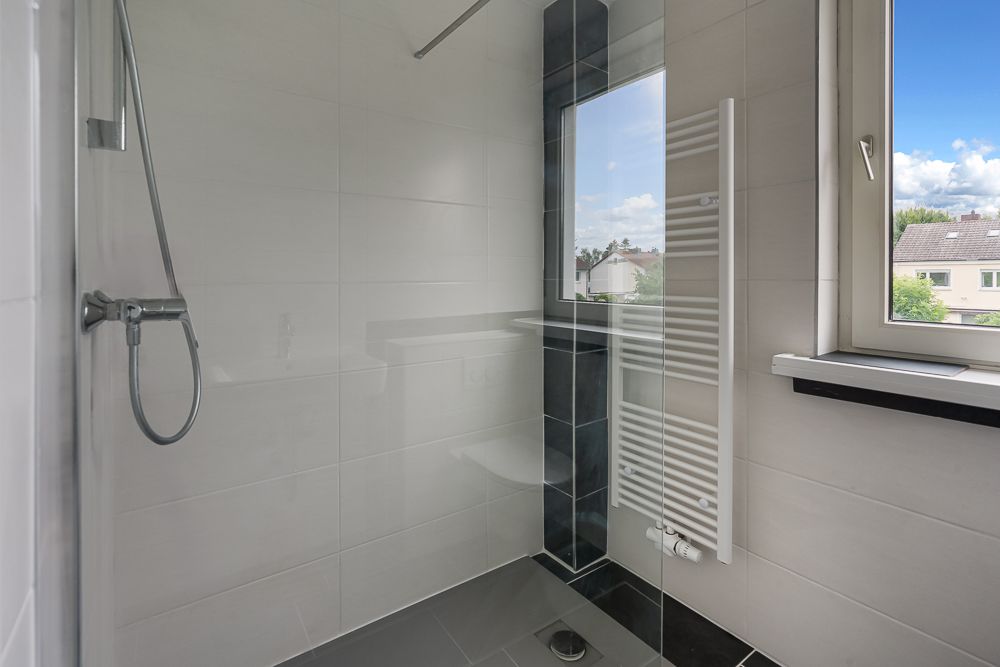 Moderne, geflieste Dusche mit Fenster und Handbrause in einem Badezimmer.