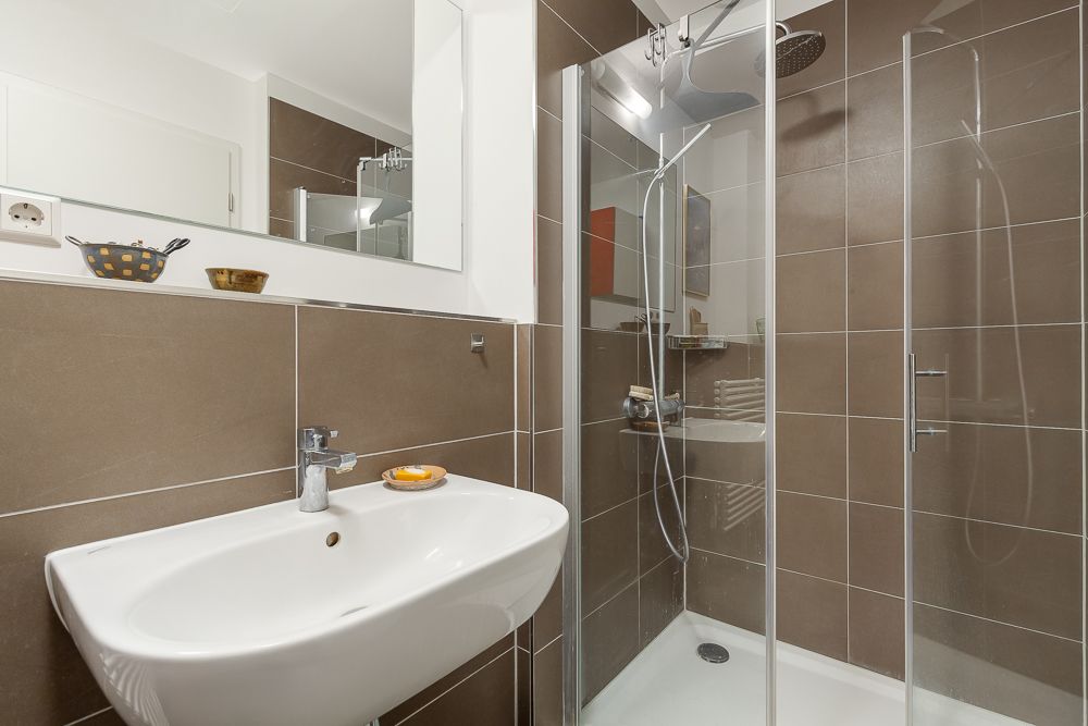 Modernes Badezimmer mit braunen Fliesen, Waschbecken, Spiegel und Glasdusche.