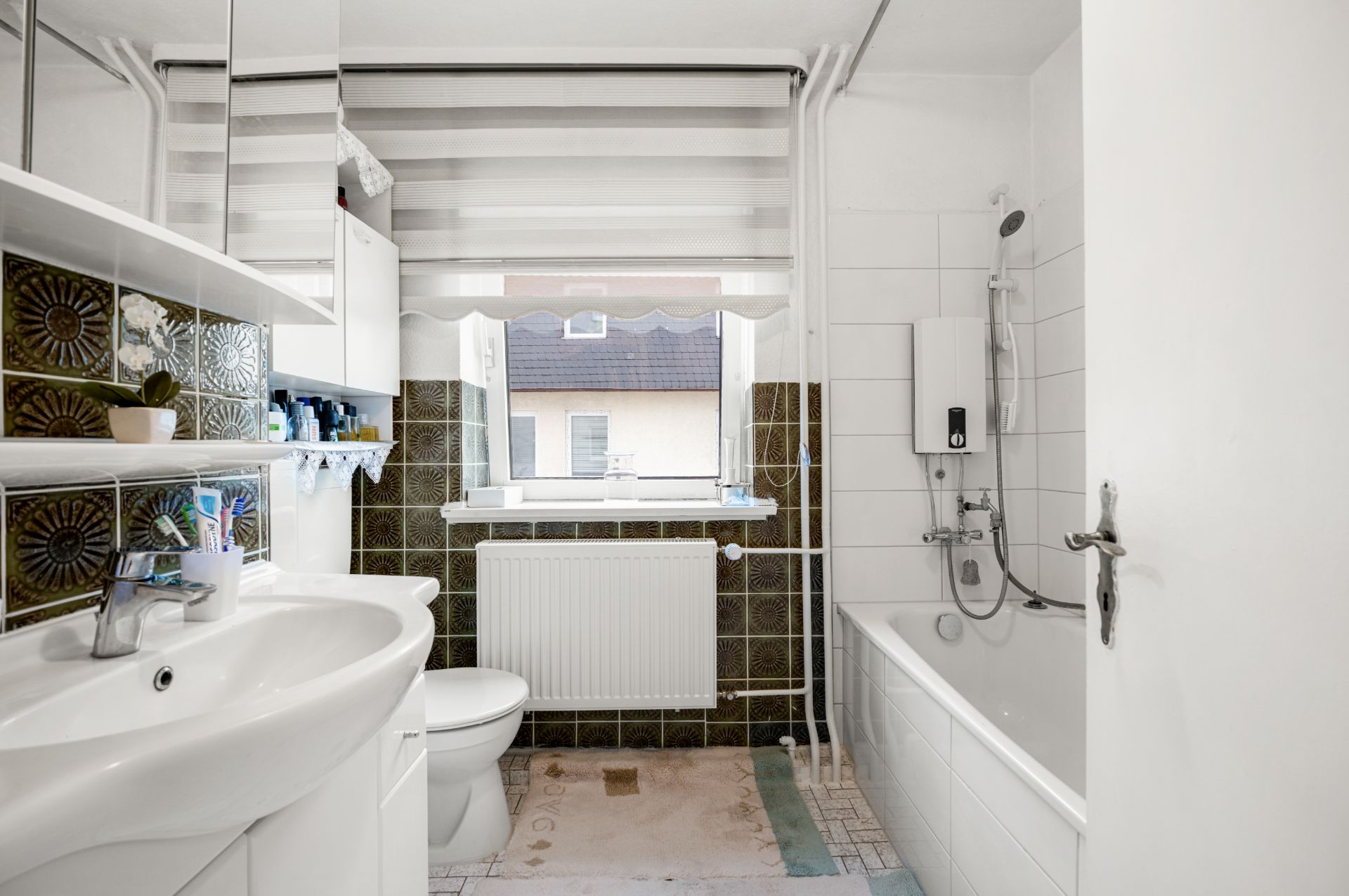 Badezimmer mit Waschbecken, Toilette, Badewanne, Heizkörper und Fenster.
