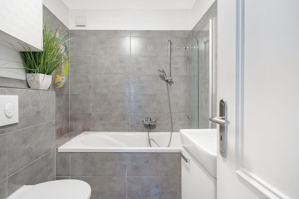 Modernes Badezimmer mit grauen Fliesen, Badewanne, Dusche, Toilette und Waschbecken.