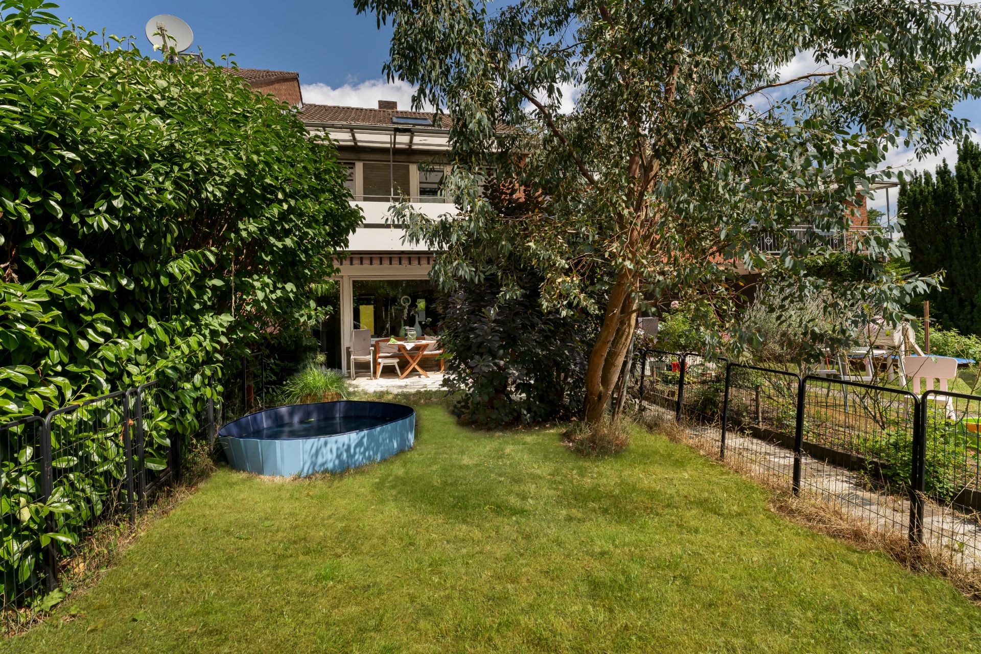 Grüner Garten mit kleinem Pool, Baum und Terrasse an einem Wohnhaus.