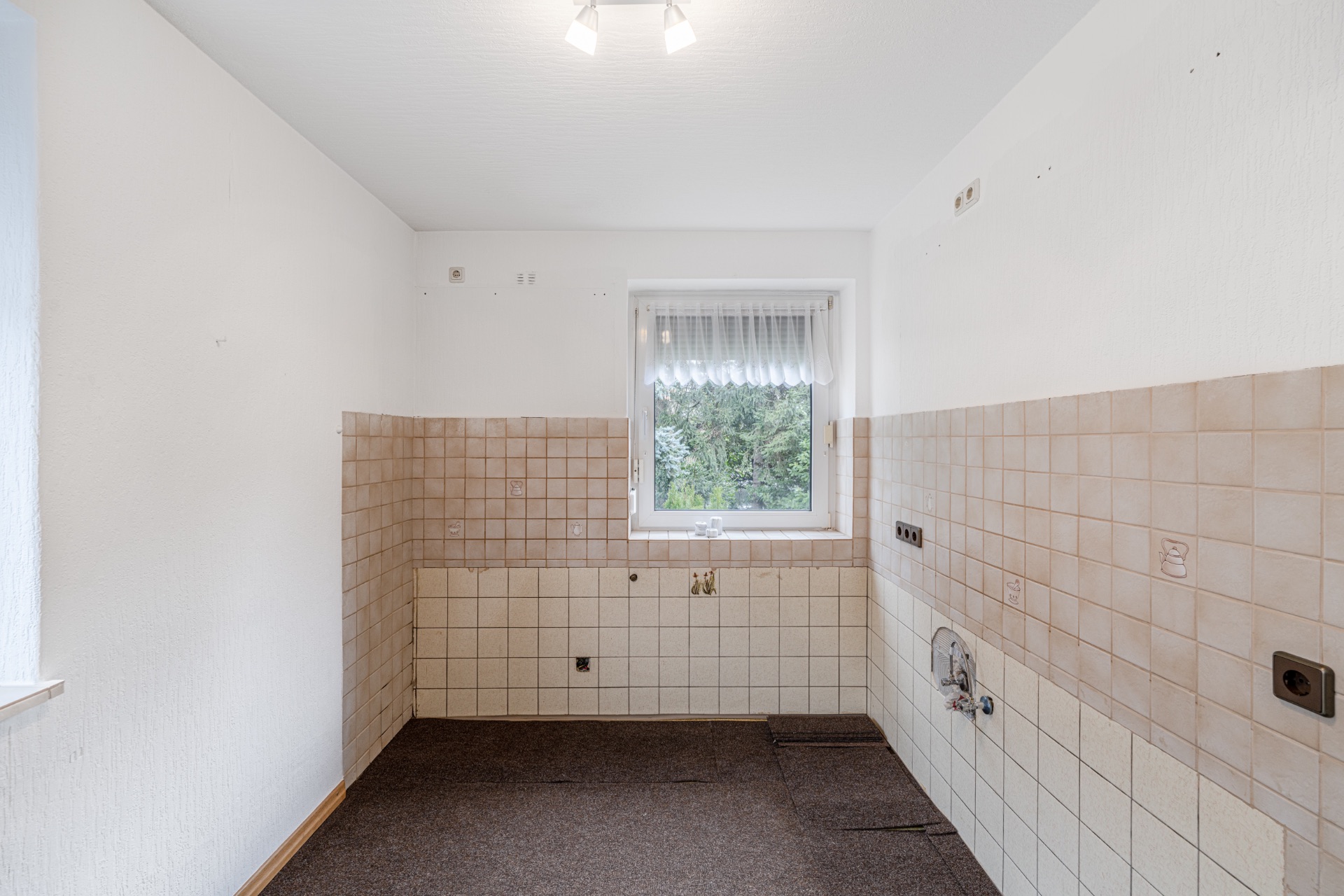 Leerer Raum mit beigen Fliesen an den Wänden und einem Fenster mit Gardine.