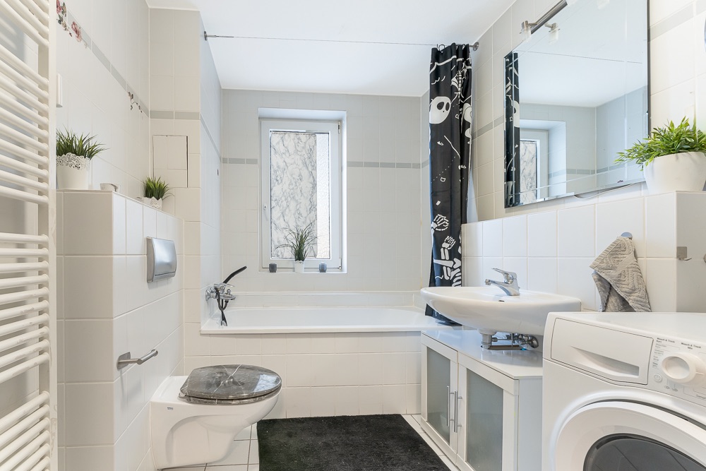 Helles Badezimmer mit Badewanne, Waschbecken, Waschmaschine, Toilette und Pflanzen.