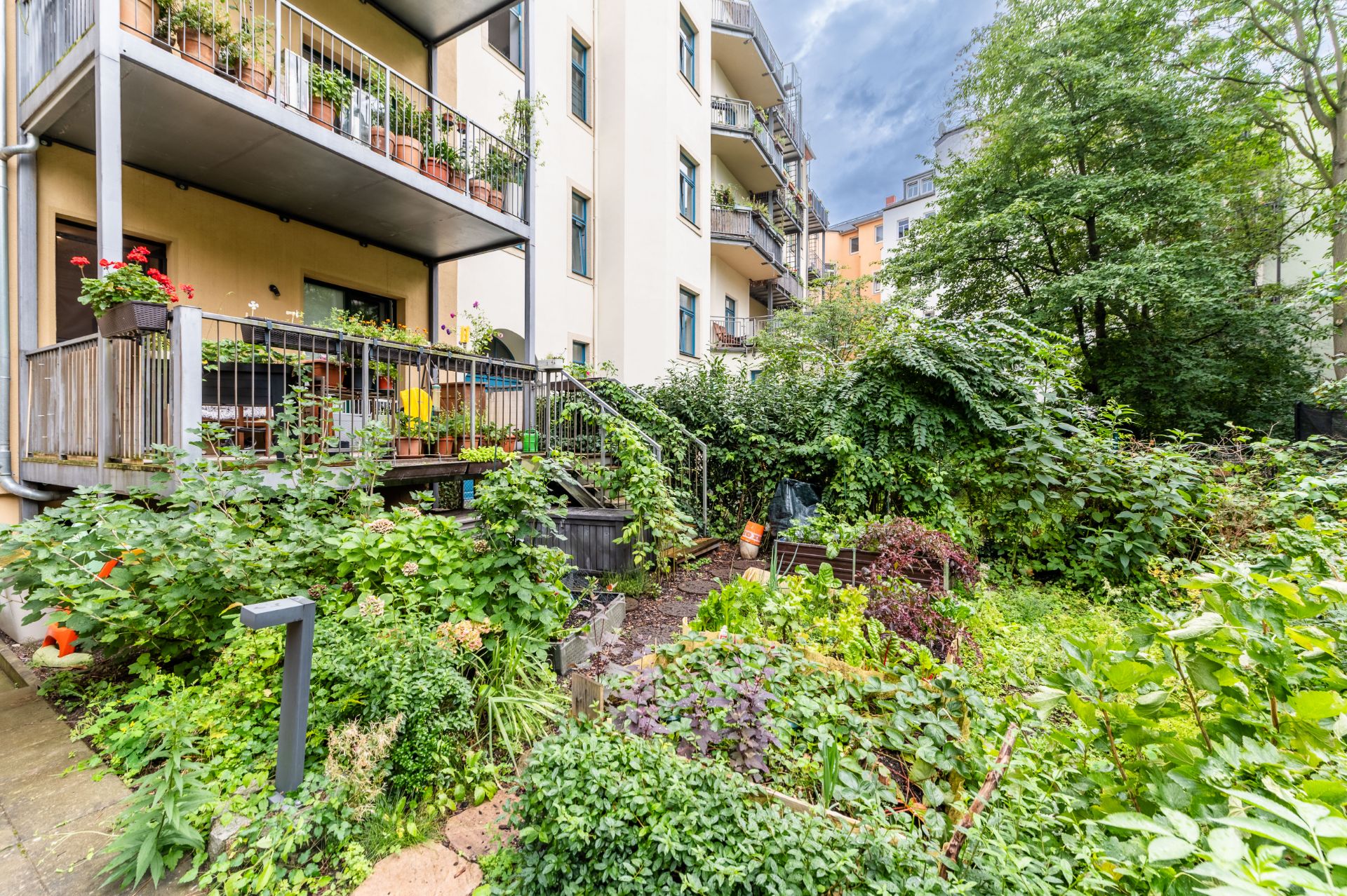 Wohnhaus mit Balkon und angrenzendem grünen Garten voller Pflanzen.