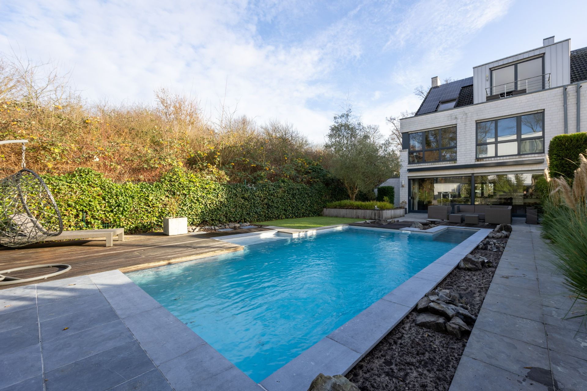 Moderner Garten mit Swimmingpool, Liegestuhl und Sitzbereich vor einem weißen Wohnhaus.