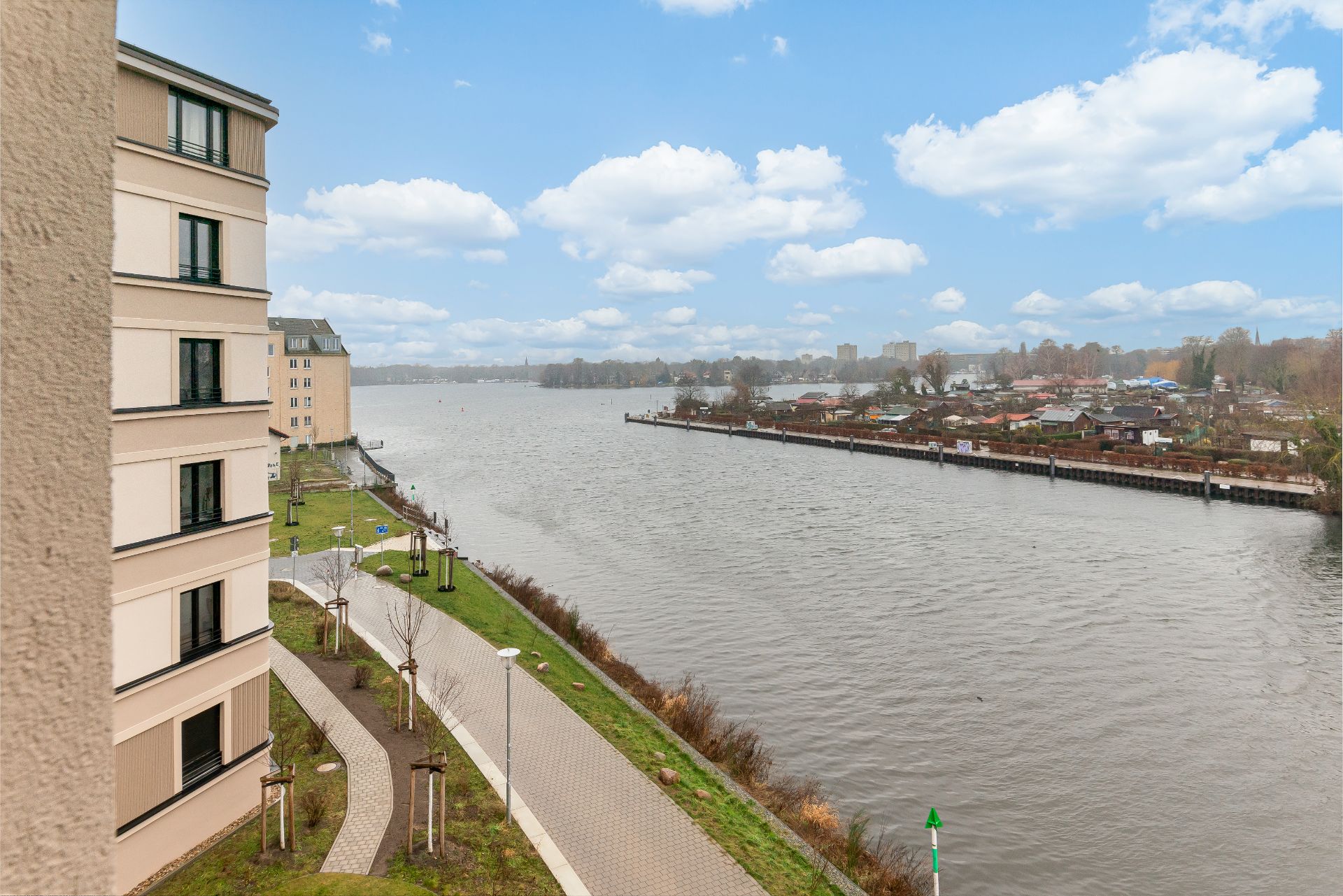 Blick von einem Wohngebäude auf einen Fluss mit Gehweg und Laternen am Ufer.