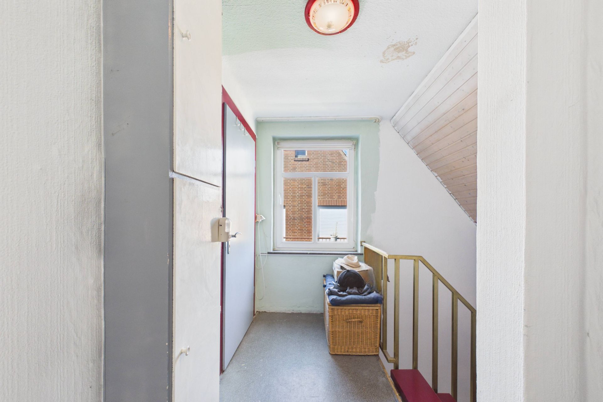 Heller Flur mit Fenster, Treppengeländer und Korb mit Kleidung neben der Treppe.