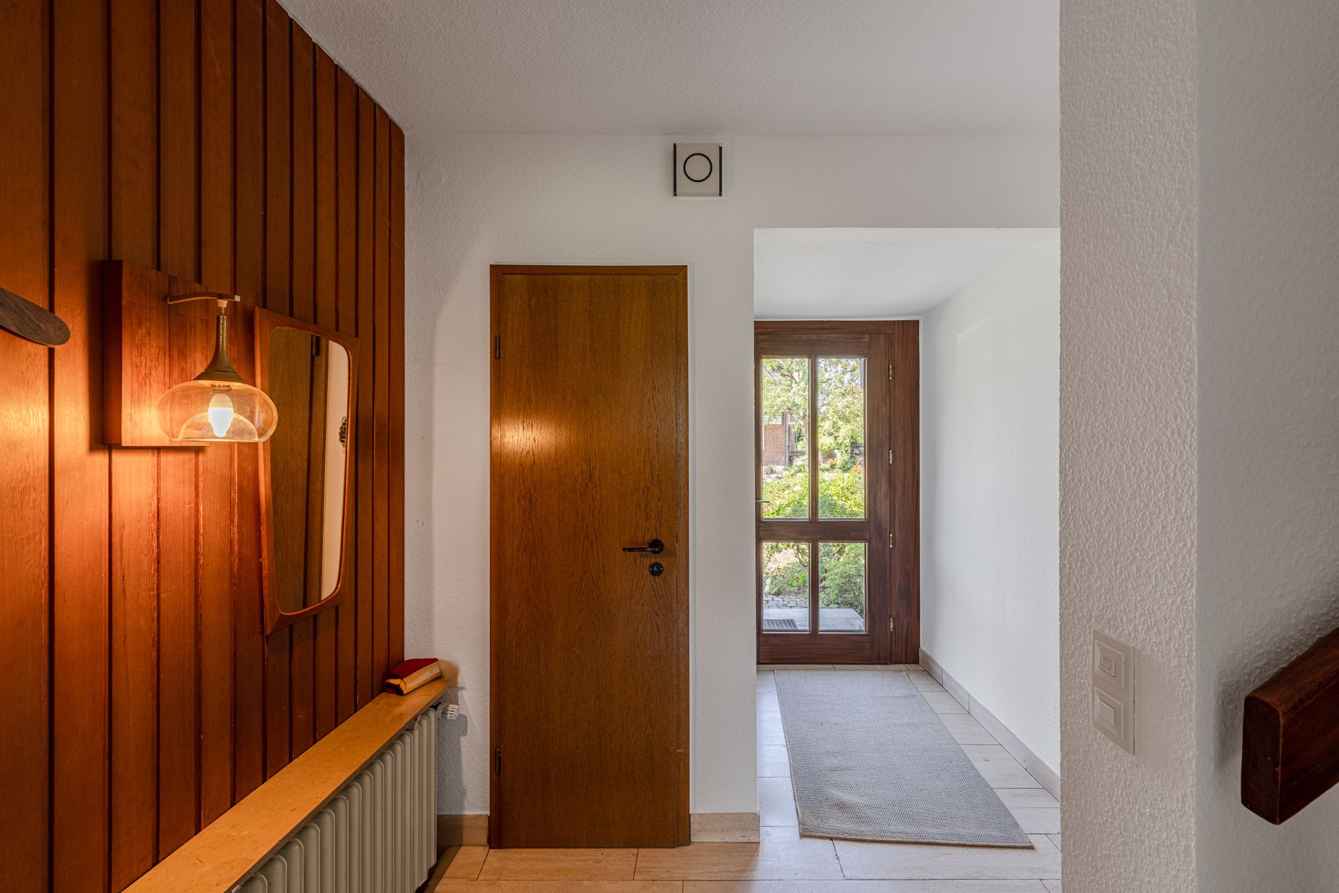 Flur mit Holztür, Fenster, Teppich und beleuchteter Holzverkleidung an der Wand.