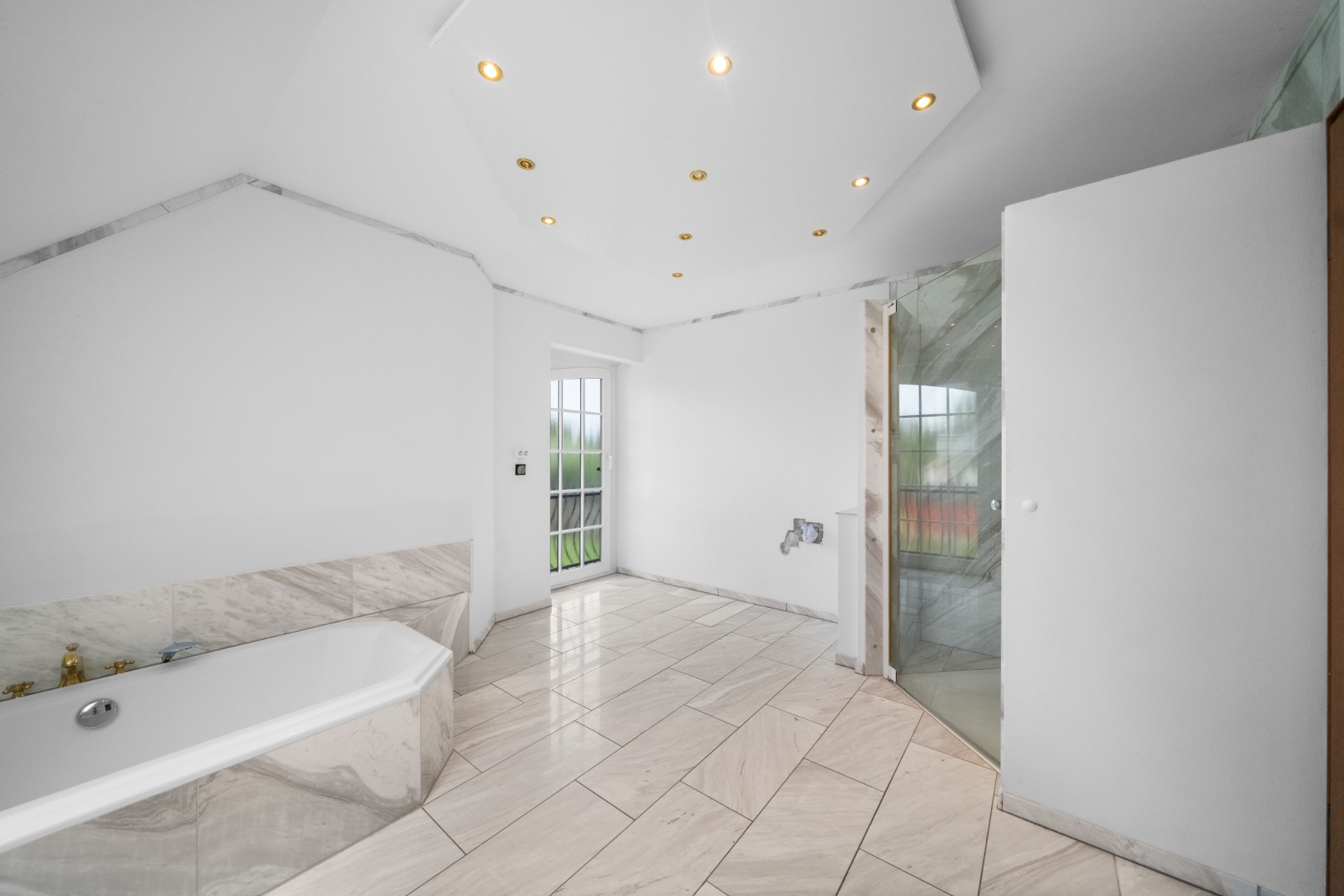 Helles Badezimmer mit Badewanne, Dusche, gefliestem Boden und Glastür zu einem Balkon.