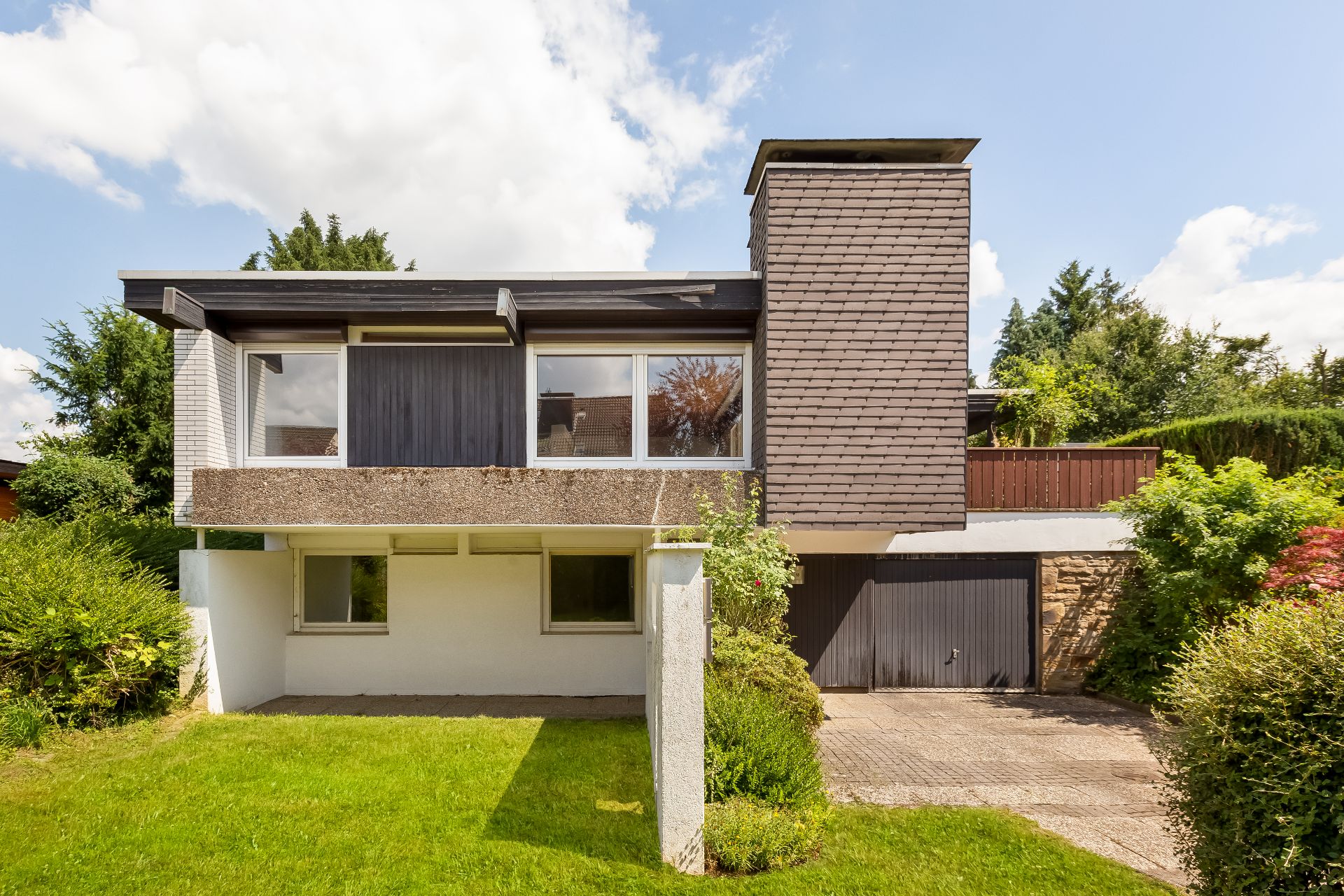Modernes Einfamilienhaus mit großem Fenster, Garage und gepflegtem Vorgarten.