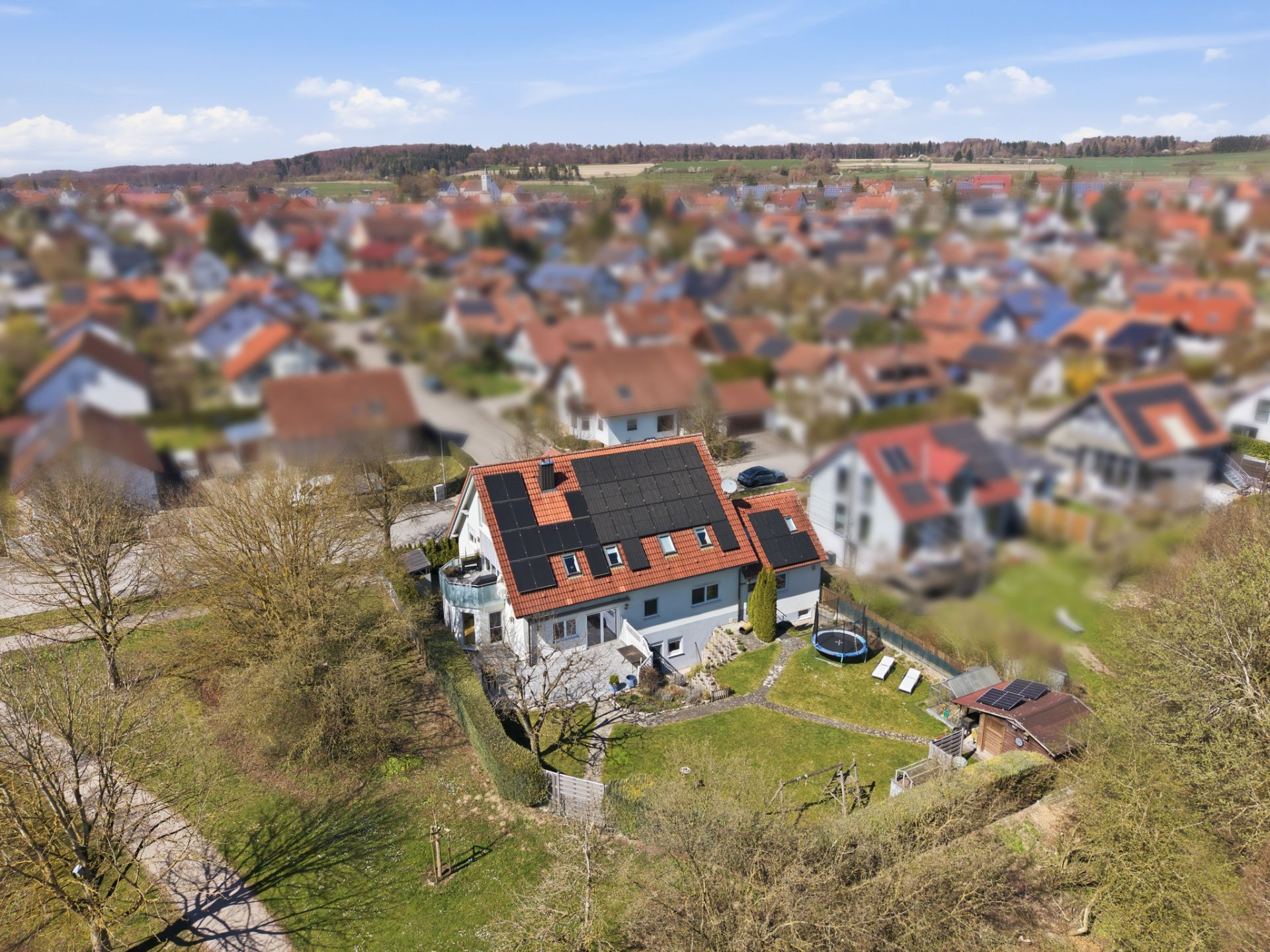 Luftaufnahme eines Hauses mit Solarpanelen und großem Garten in einem Wohngebiet.