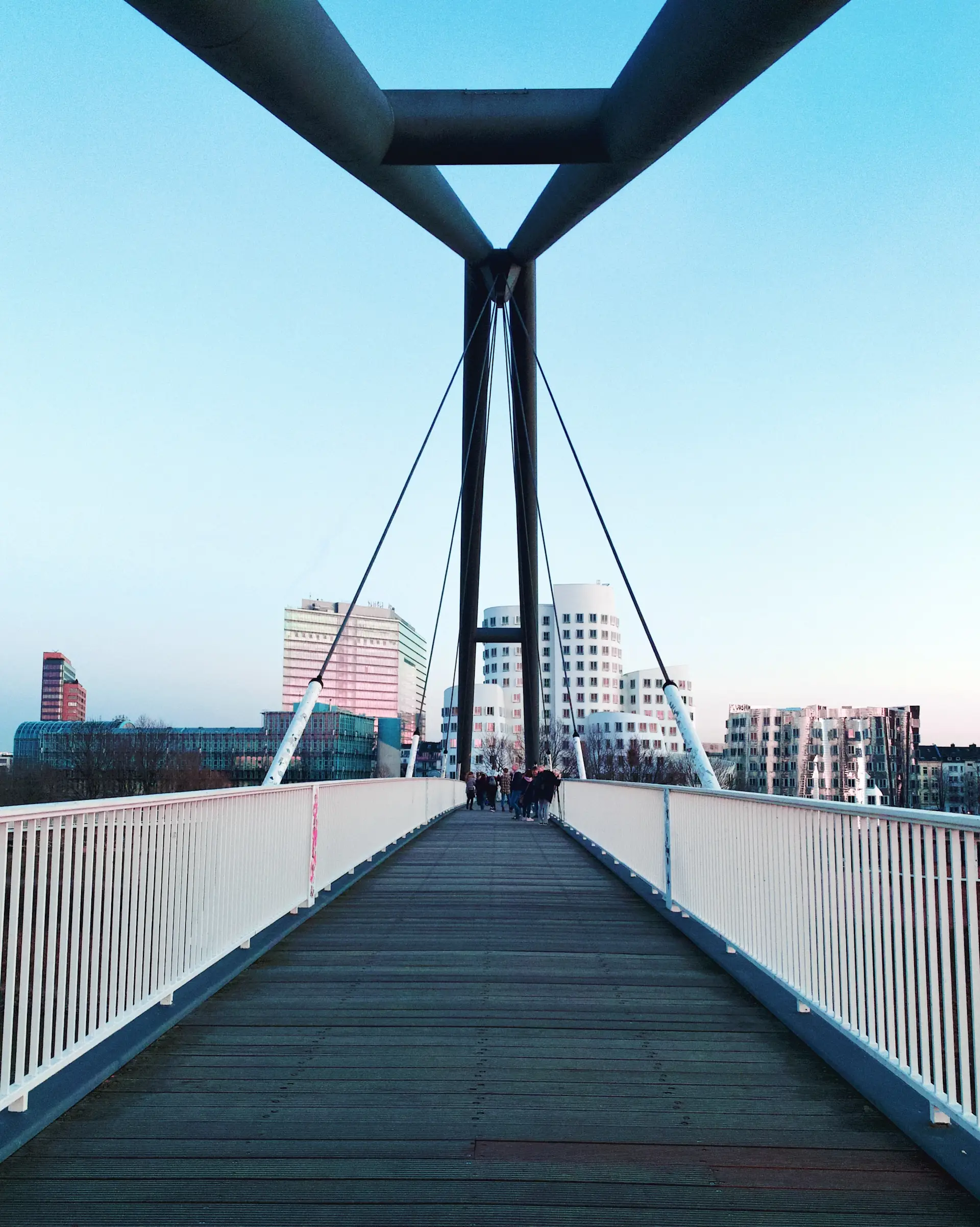 Fußgängerbrücke mit weißen Geländern und modernen Gebäuden im Hintergrund.