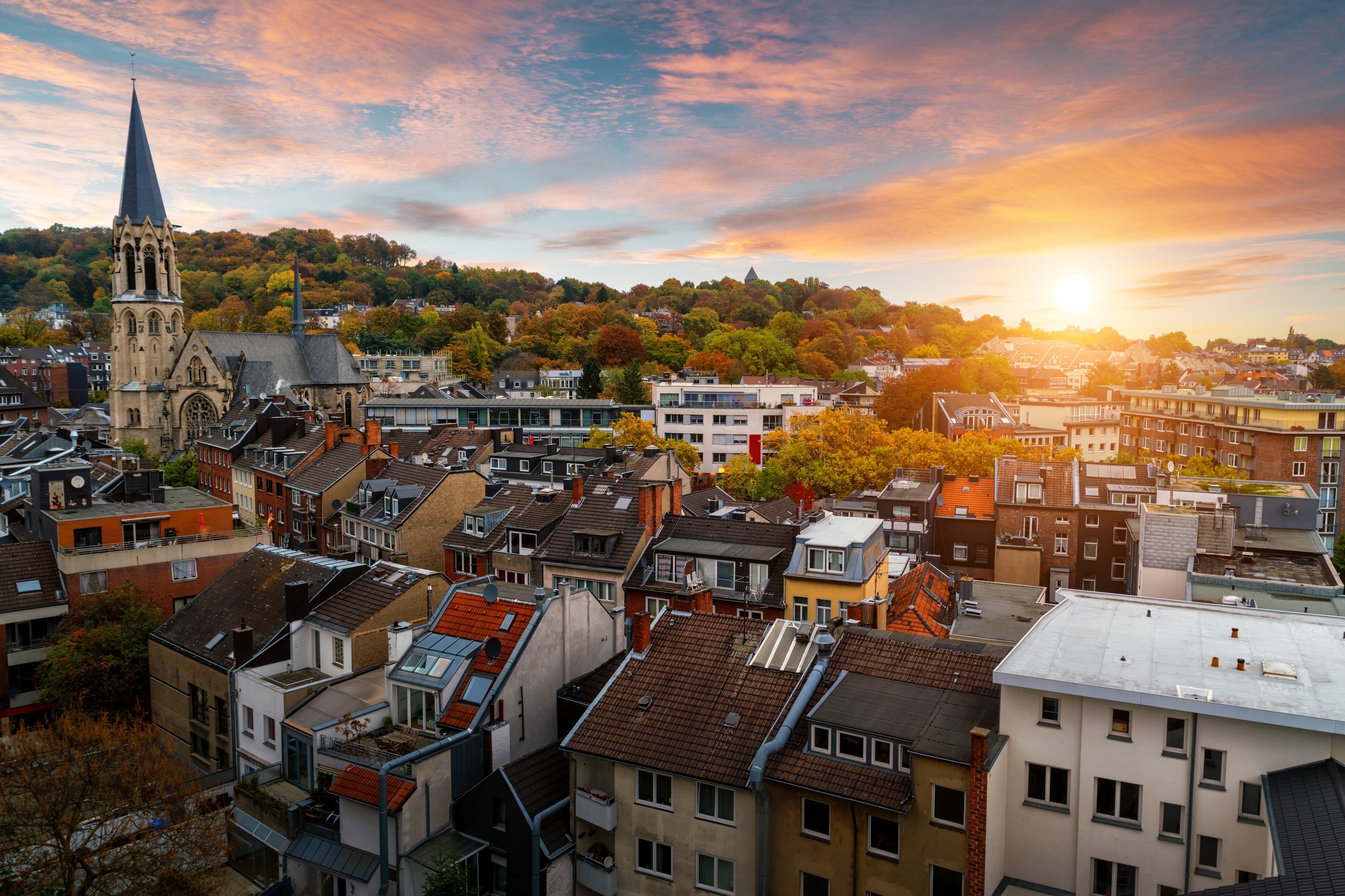 Stadtansicht mit Wohnhäusern, einer Kirche und Sonnenuntergang im Hintergrund.