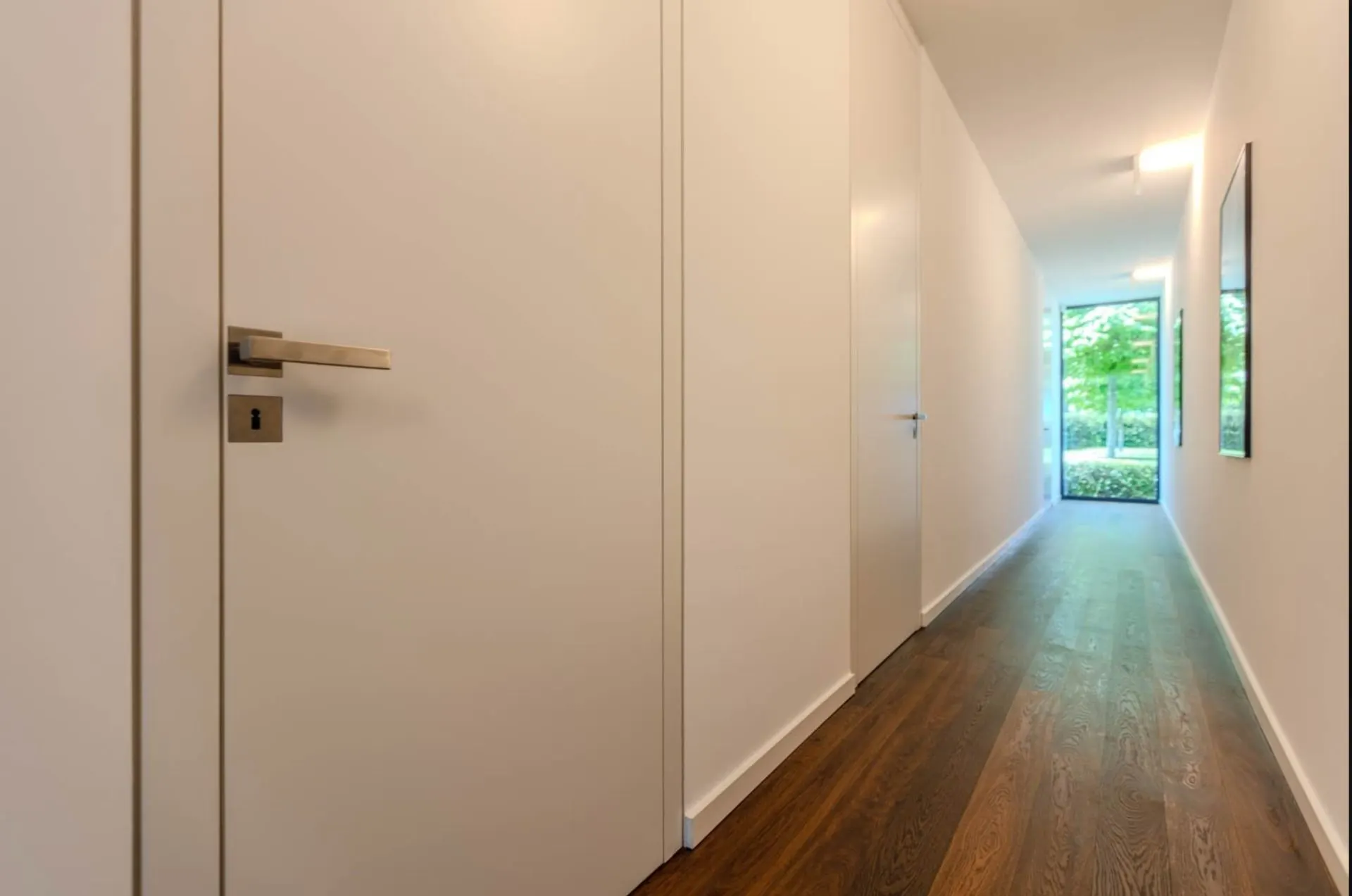 Langer, heller Flur mit Holzboden, weißen Wänden und Fenstertür am Ende.