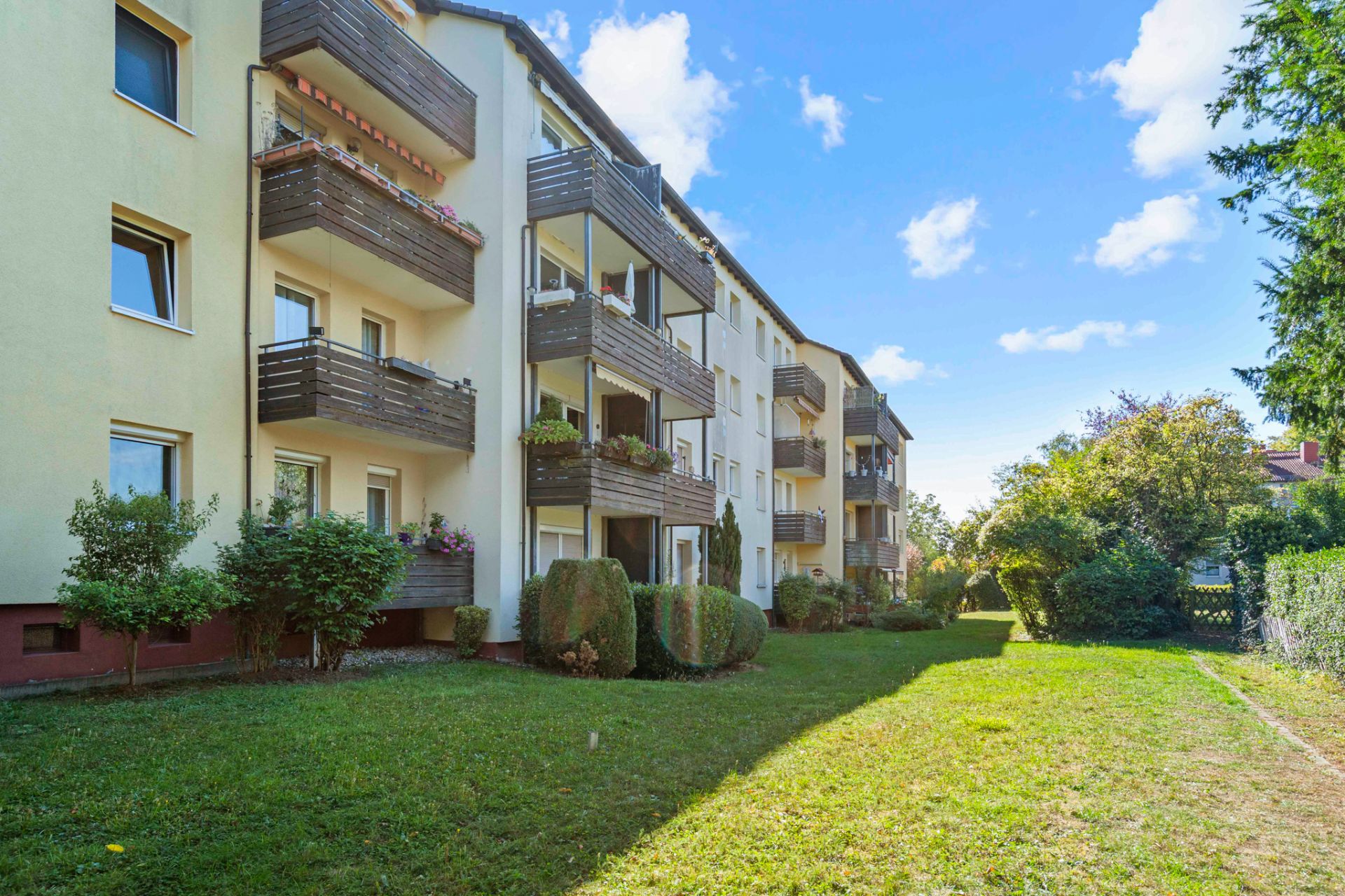 Mehrfamilienhaus mit mehreren Balkonen und gepflegtem Gartenbereich.
