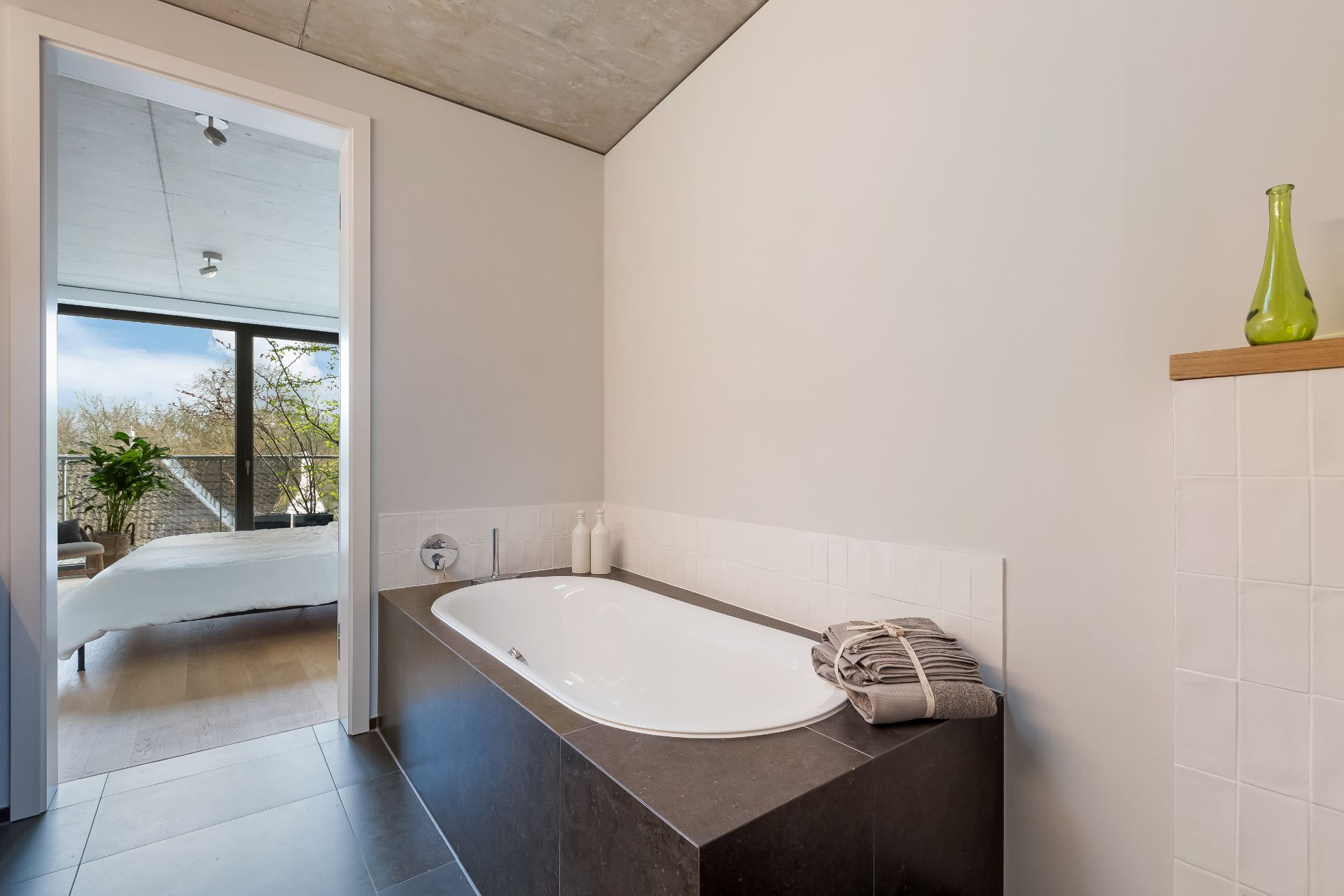 Modernes Badezimmer mit Badewanne, Handtüchern und Zugang zu einem Schlafzimmer mit Balkon.