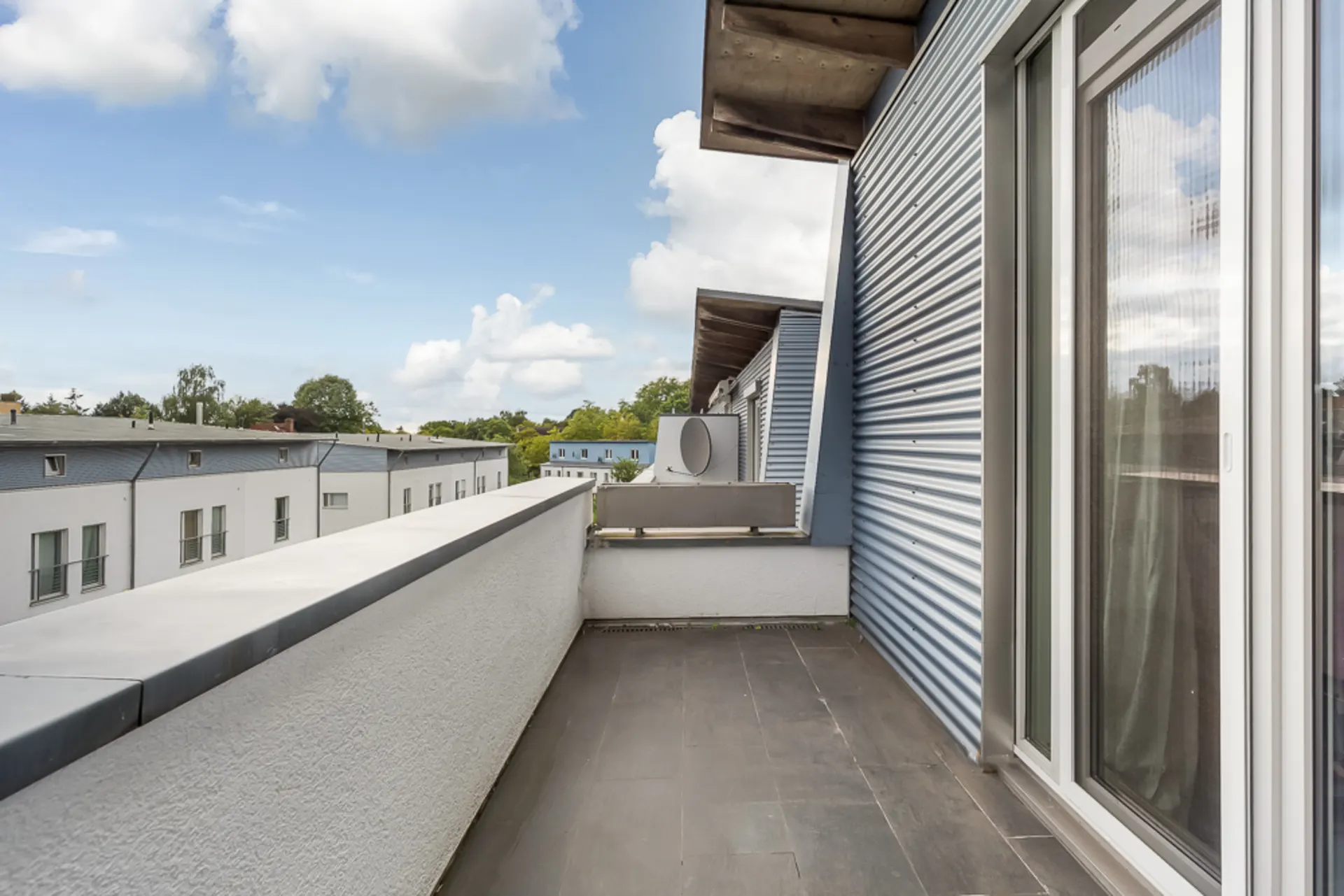 Balkon mit Fliesenboden und weißer Brüstung, seitlich an einem Wohngebäude gelegen.