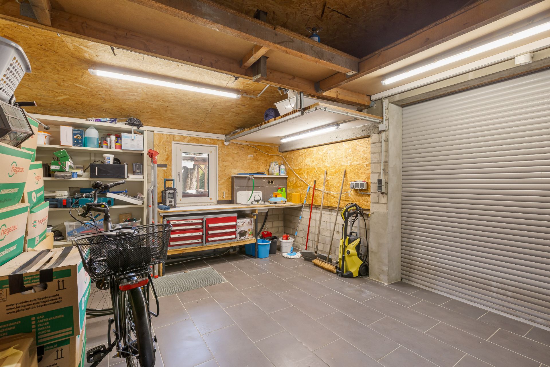 Aufgeräumte Garage mit Regalen, Werkbank, Fahrrad und Reinigungsgeräten.
