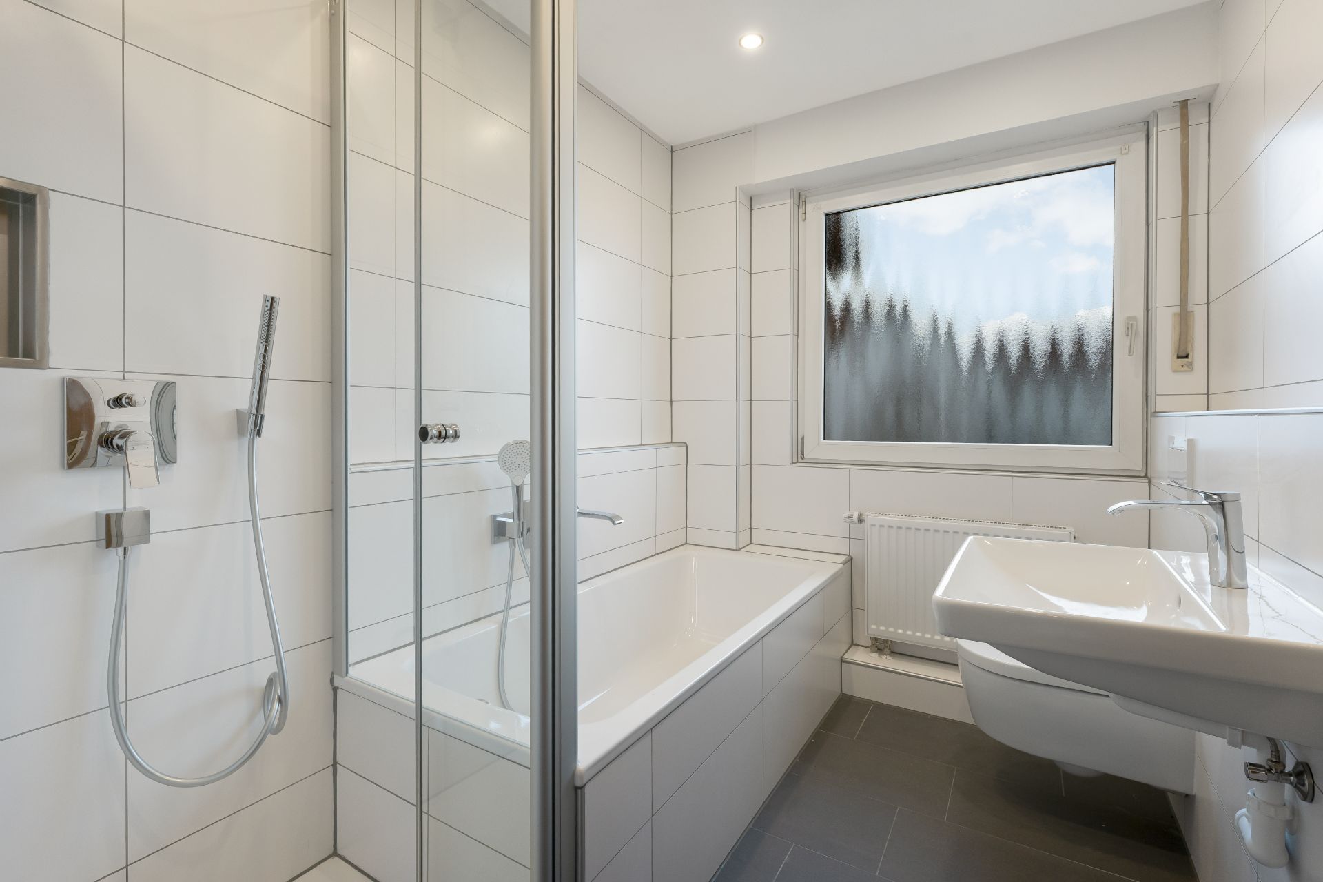 Modernes Badezimmer mit Badewanne, Dusche, Waschbecken und großem Fenster.
