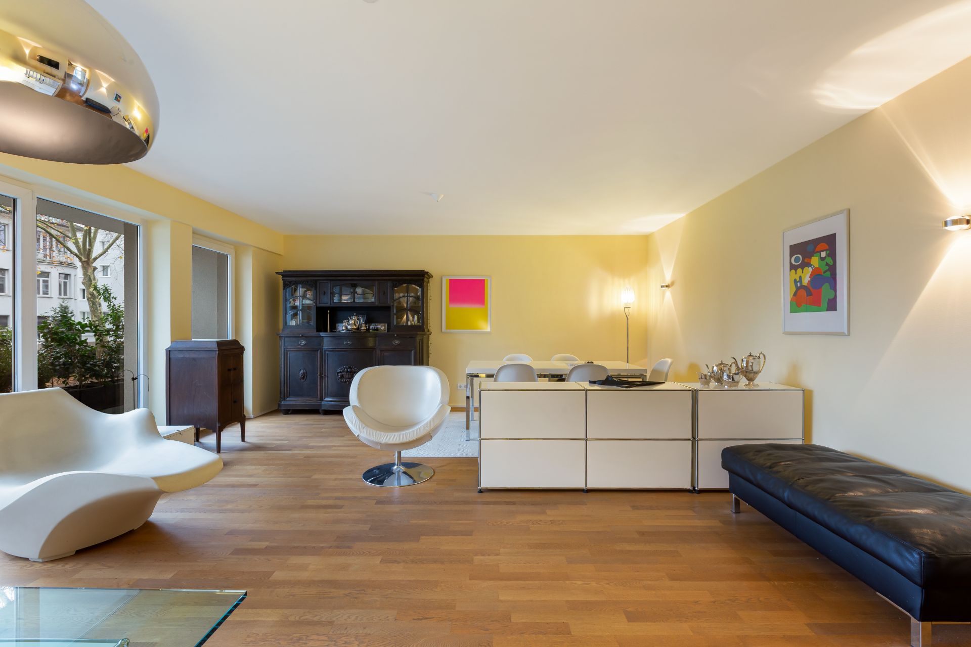 Modernes Wohnzimmer mit Holzboden, weißen Möbeln, schwarzem Schrank und großer Fensterfront.
