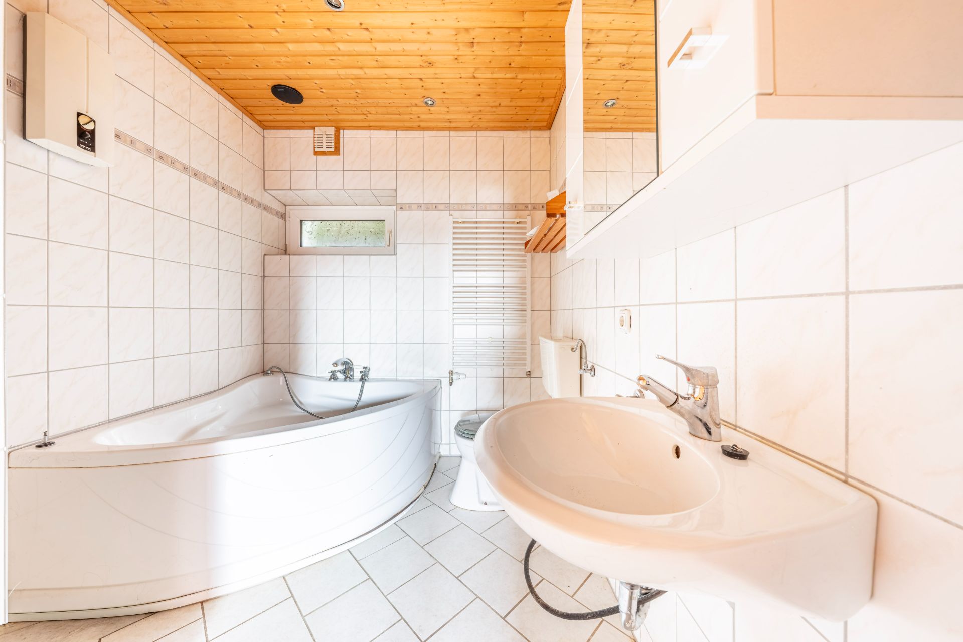 Modernes Badezimmer mit Eckbadewanne, Waschbecken, Toilette und Holzdecke.