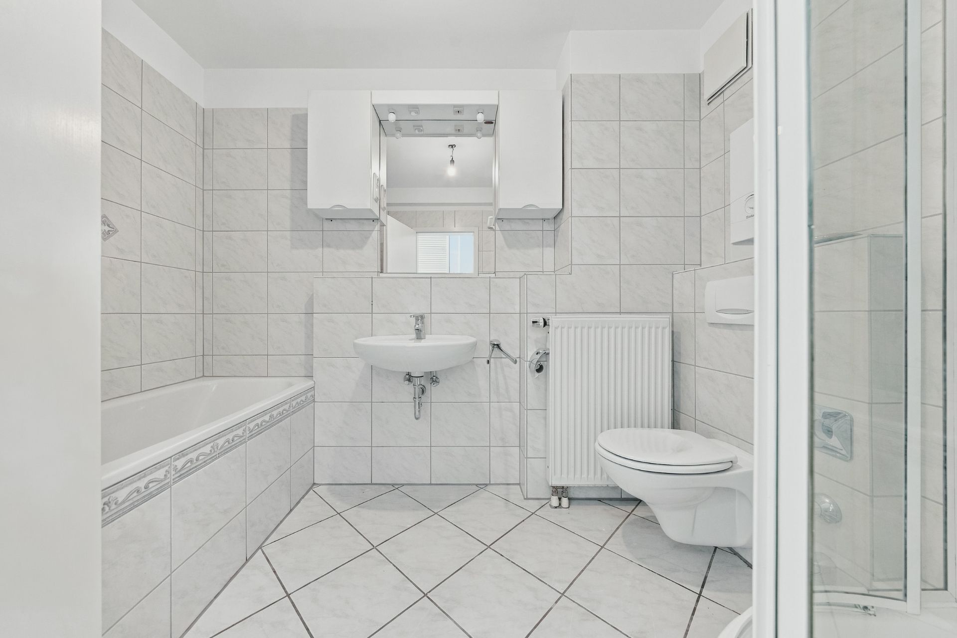 Helles Badezimmer mit Badewanne, Waschbecken, Toilette, Dusche und Spiegel, alles gefliest.