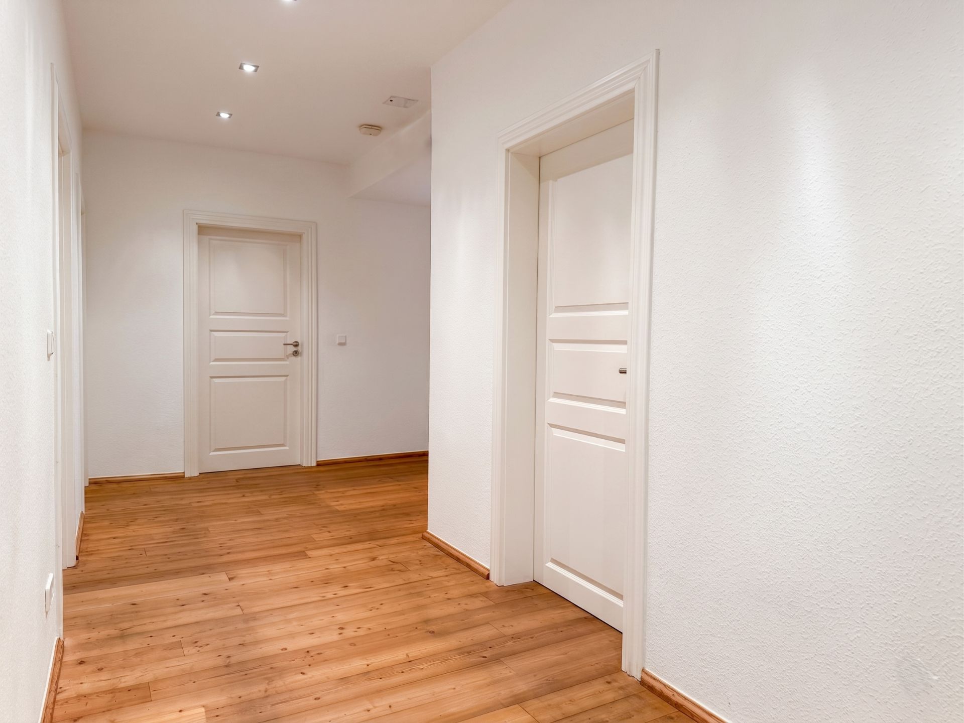 Heller Flur mit Holzboden und weißen Türen in einer Wohnung.