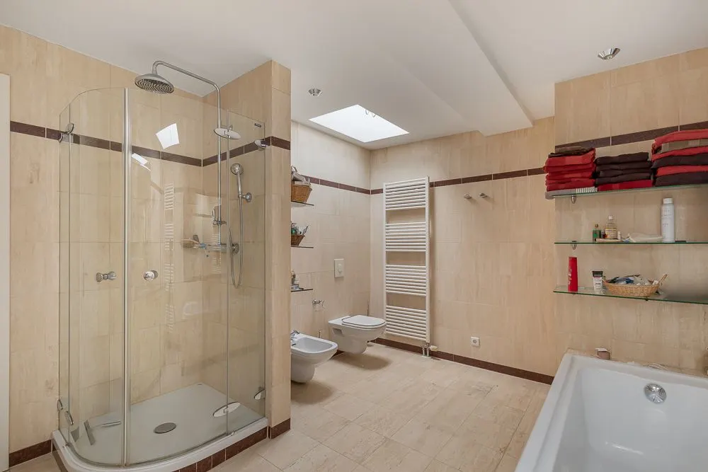 Modernes Badezimmer mit Dusche, Badewanne, WC, Bidet, Handtuchheizkörper und Regal mit Handtüchern.
