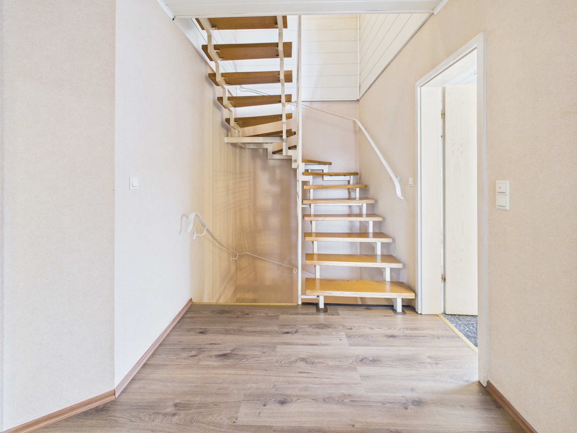 Helle Treppe mit Holzstufen und weißem Geländer in einem Flur mit Holzboden.