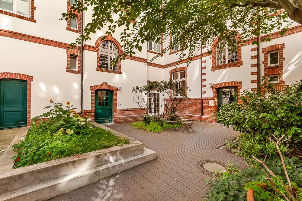 Innenhof mit Pflanzenbeeten, Sitzgruppe und Backsteinfassade eines Wohnhauses.