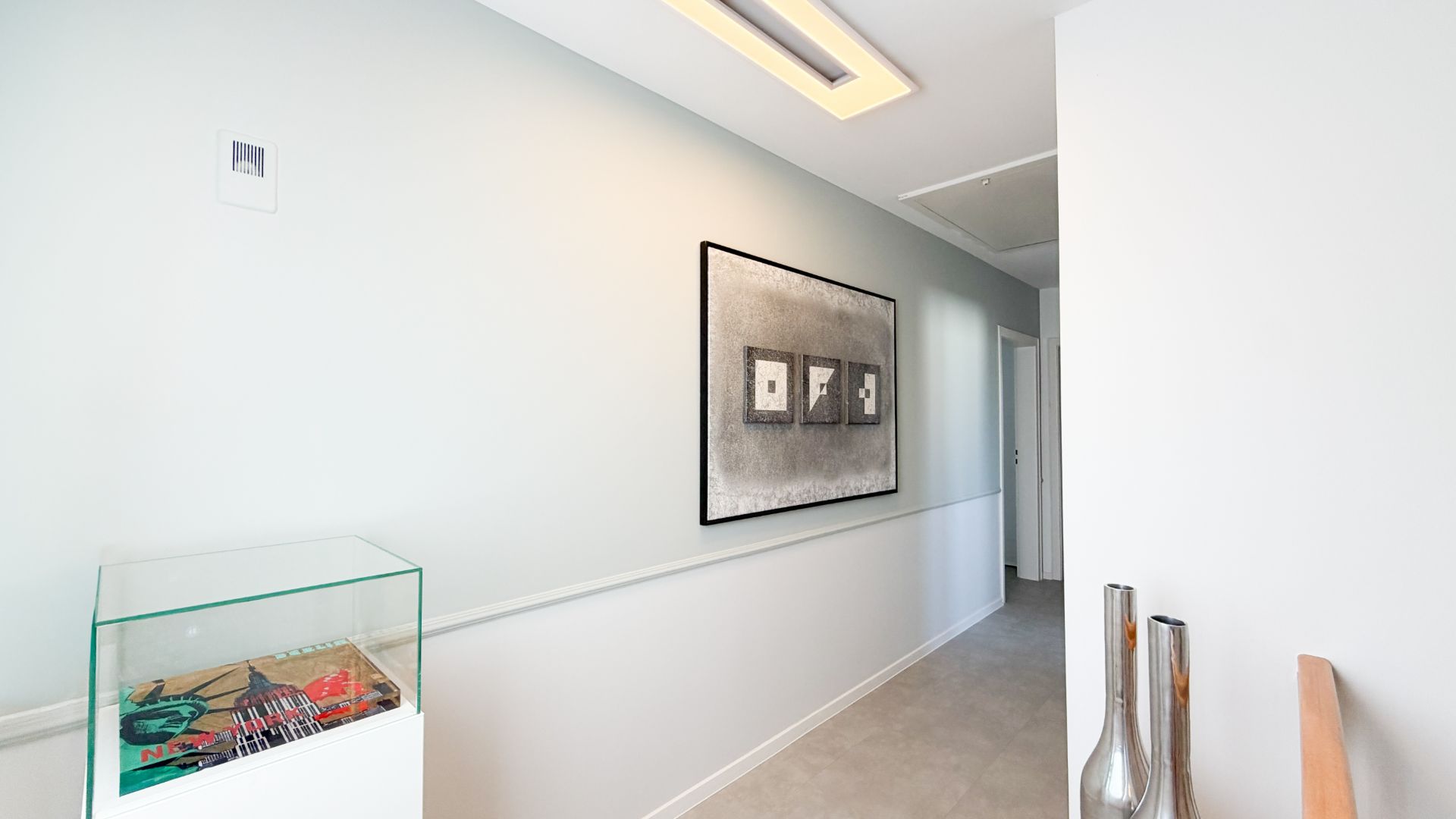 Heller Flur mit modernem Bild an der Wand und Glasvitrine links.