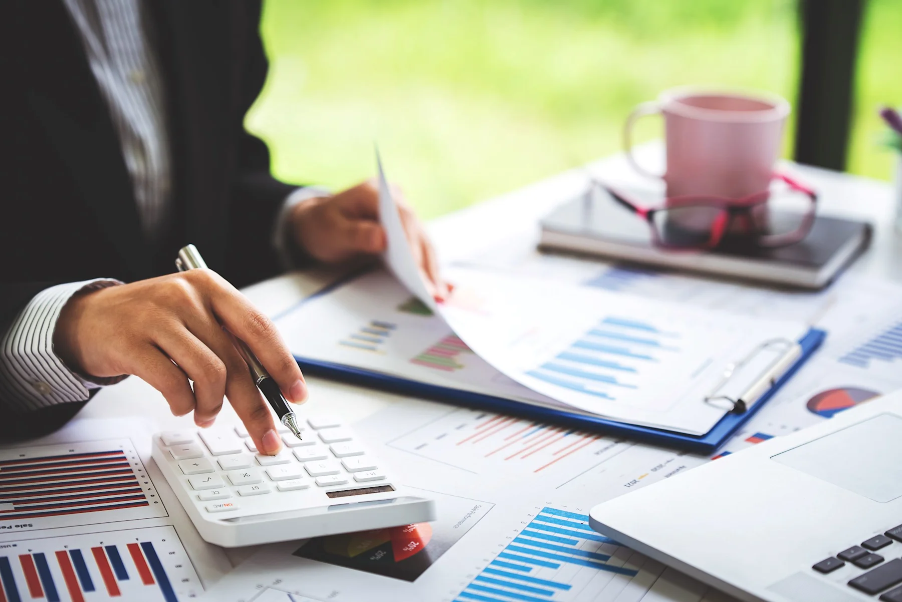 Person arbeitet mit Taschenrechner, Stift und Diagrammen an einem Schreibtisch.
