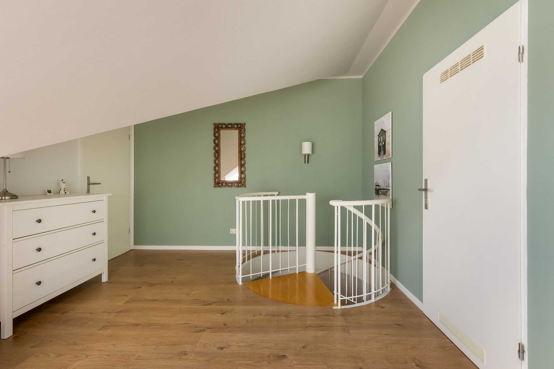 Heller Flur mit Holzfußboden, weißer Kommode und runder Wendeltreppe.